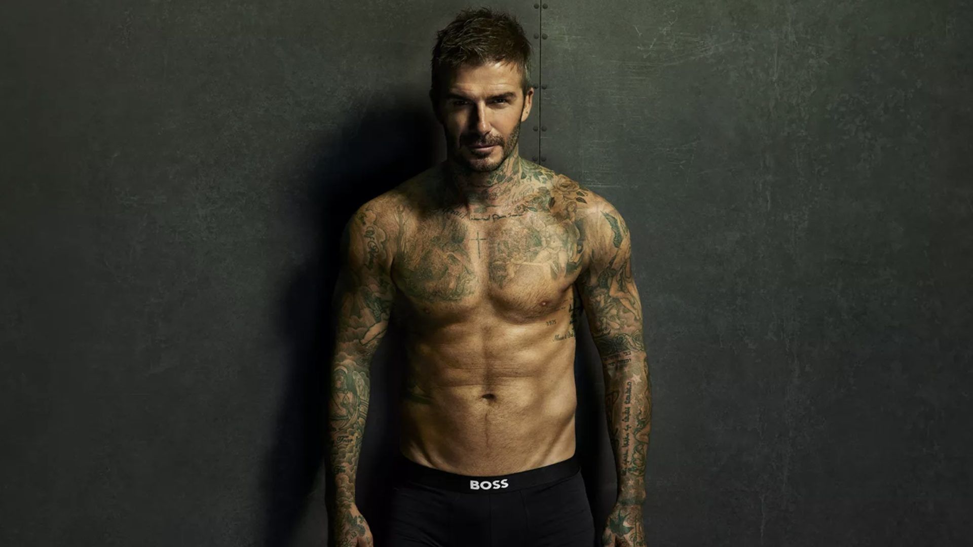 David Beckham in black boxers stands against the wall, chiseled abs