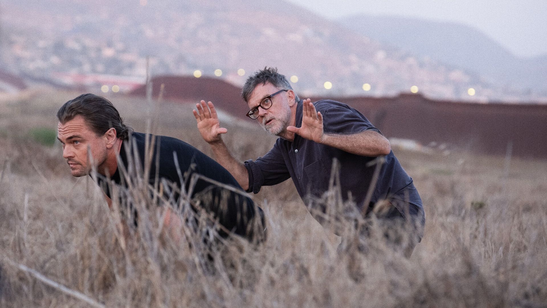 Paul Thomas Anderson and Leonardo DiCaprio walking crouched down through tall grass