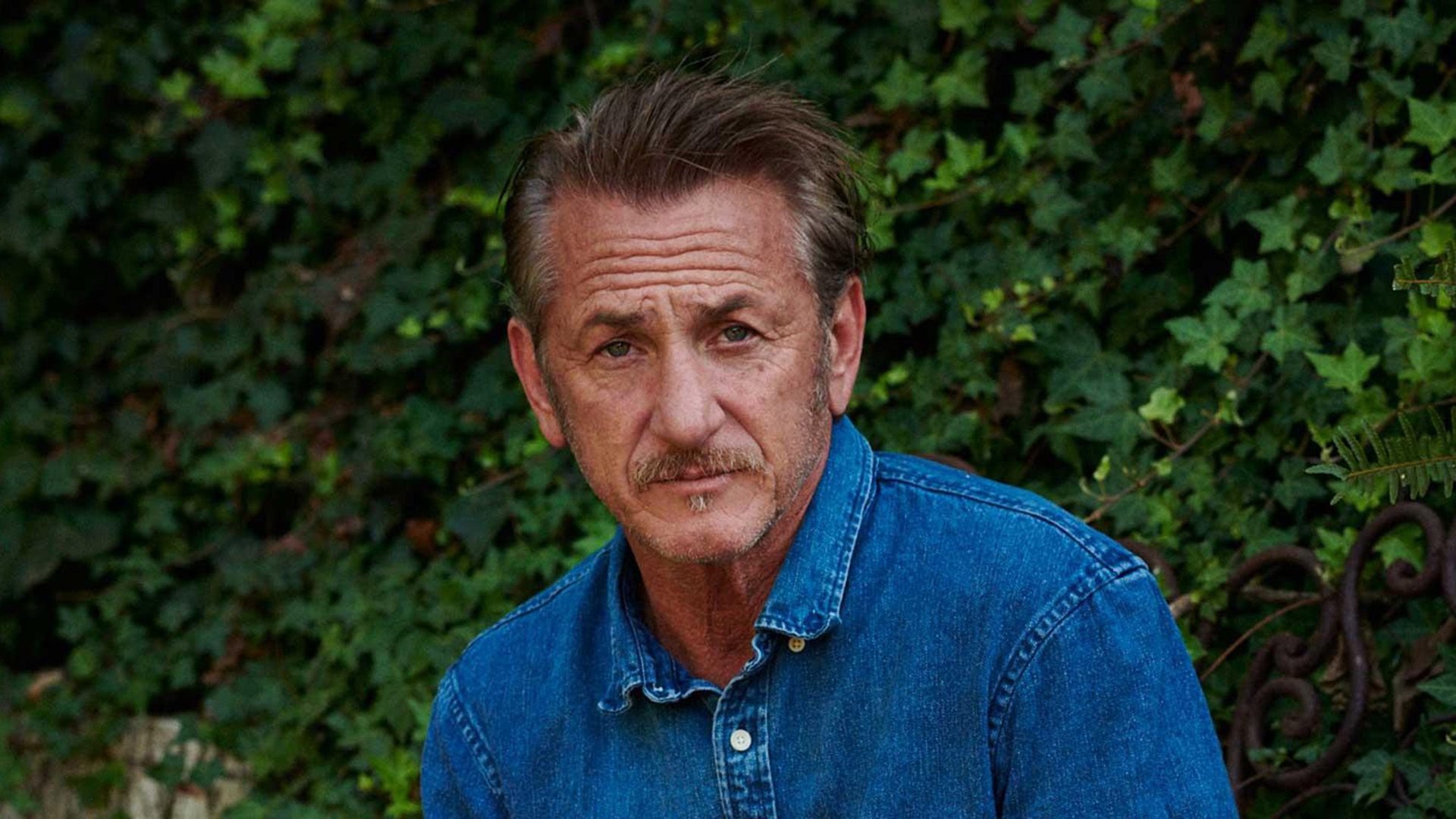 Sean Penn in a denim shirt against a backdrop of green ivy