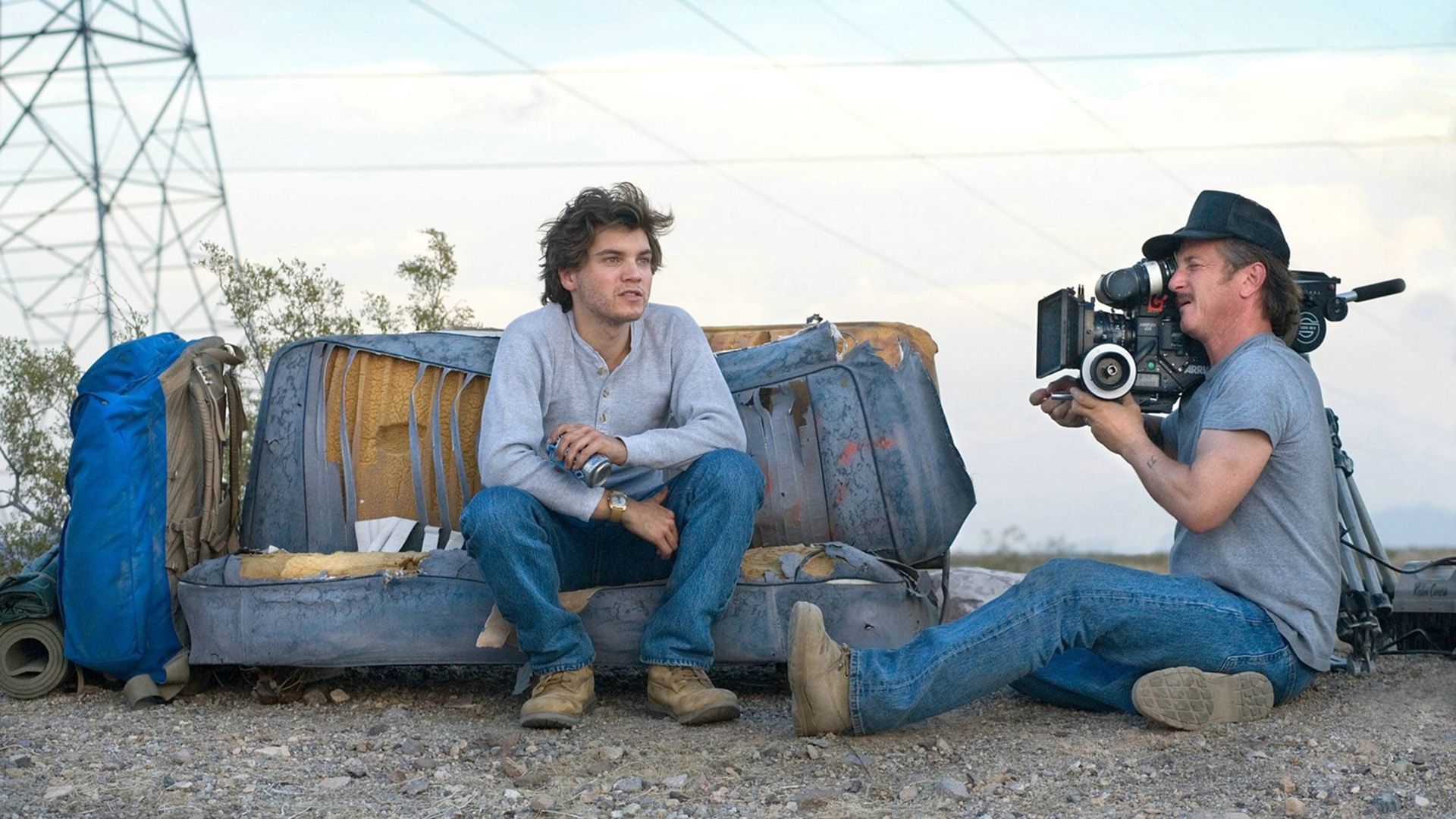 Sean Penn sitting on the ground filming a young man on a broken-down couch with a movie camera