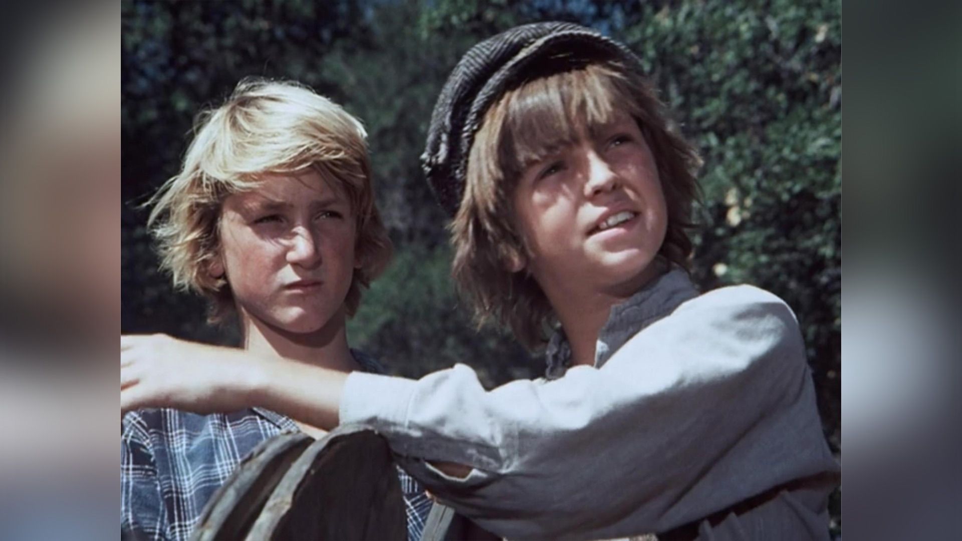 Young Sean Penn in a plaid shirt next to a boy in a gray cap