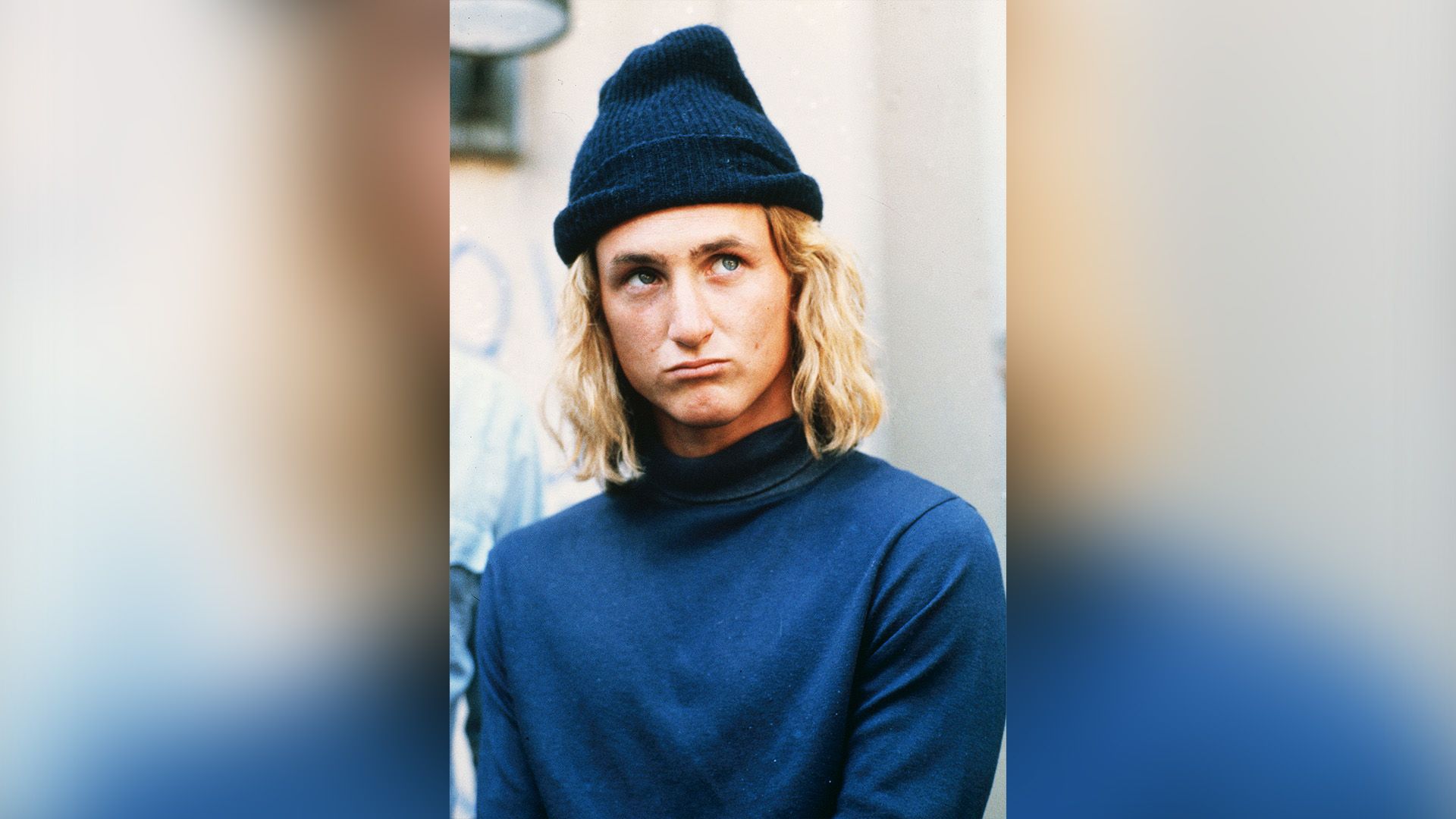 Young Sean Penn with long hair, wearing a blue turtleneck and a blue beanie