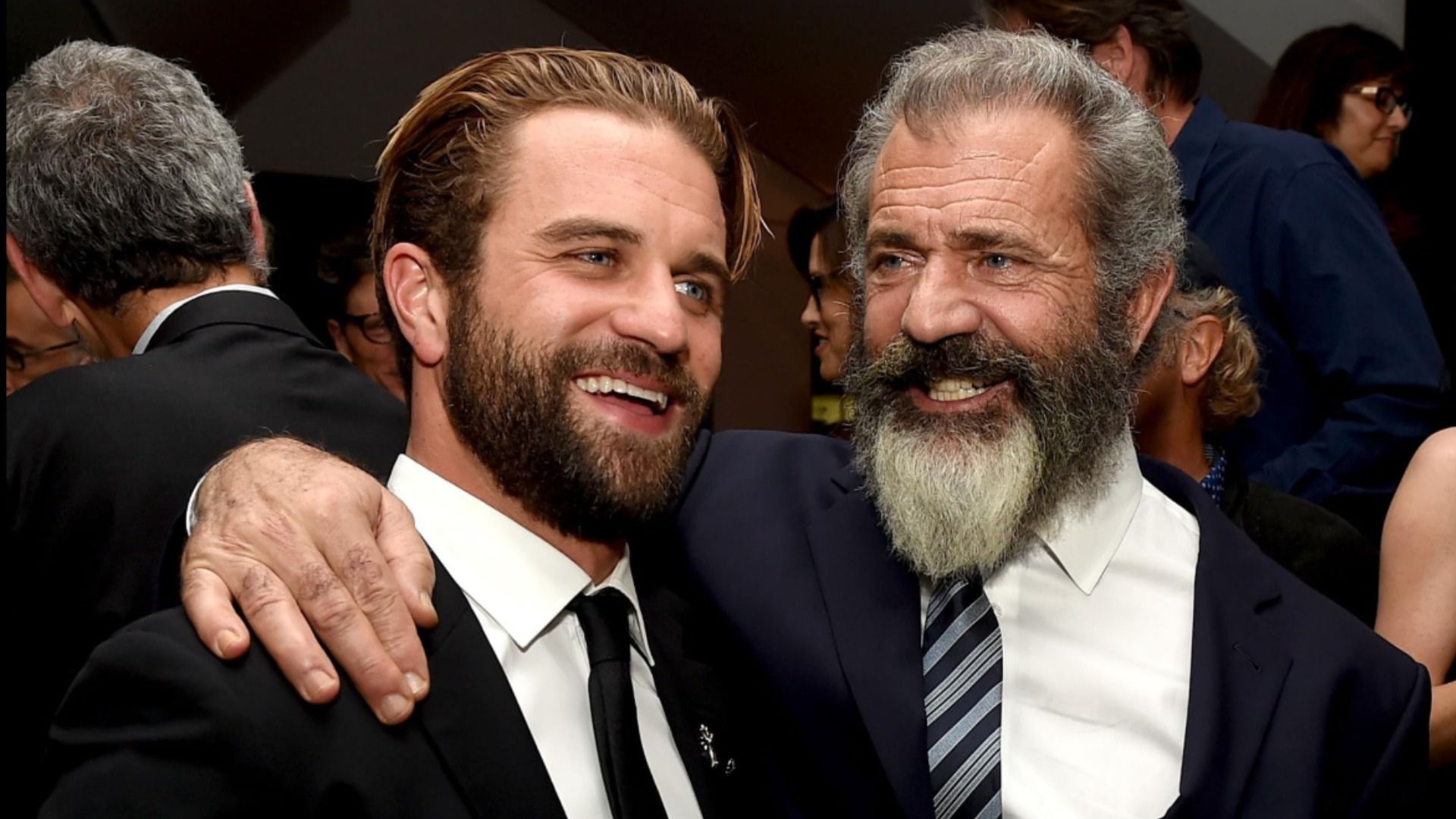 Actors Milo and Mel Gibson embrace in black suits