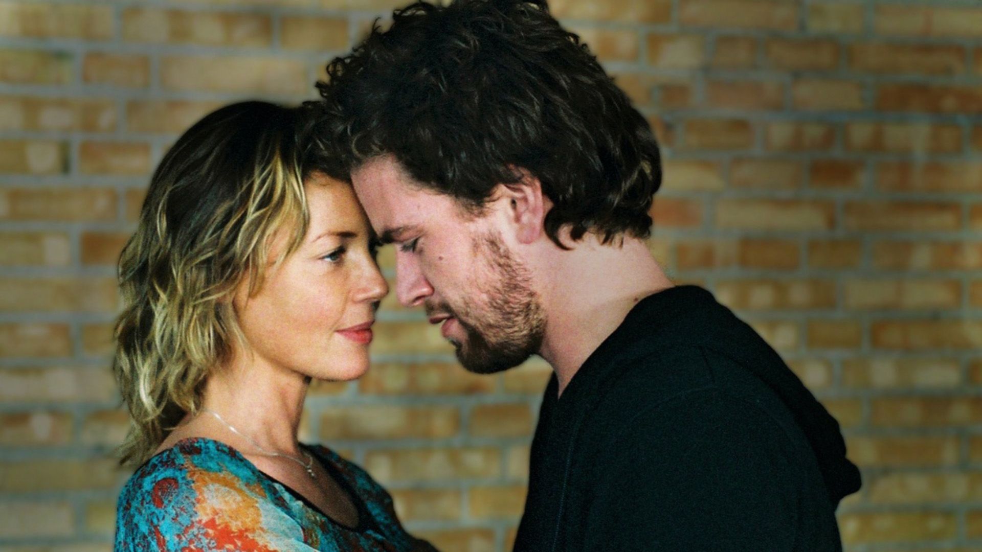 Connie Nielsen and a dark-haired man press their foreheads together