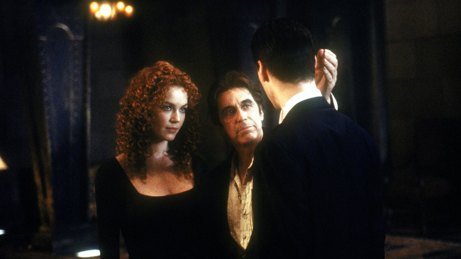 Connie Nielsen with long curly hair stands next to Al Pacino talking to Keanu Reeves