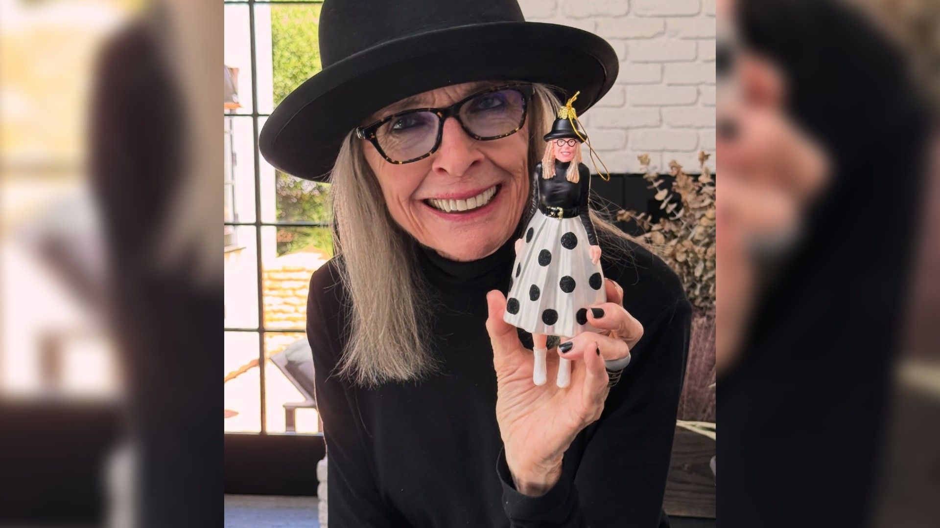 Diane Keaton in a hat showing off a Christmas ornament that's her exact replica