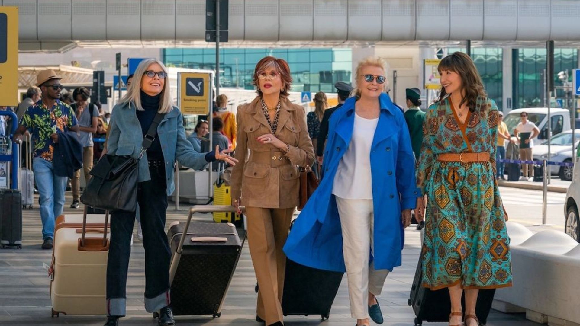 Four elegantly dressed older women walking through an airport with luggage