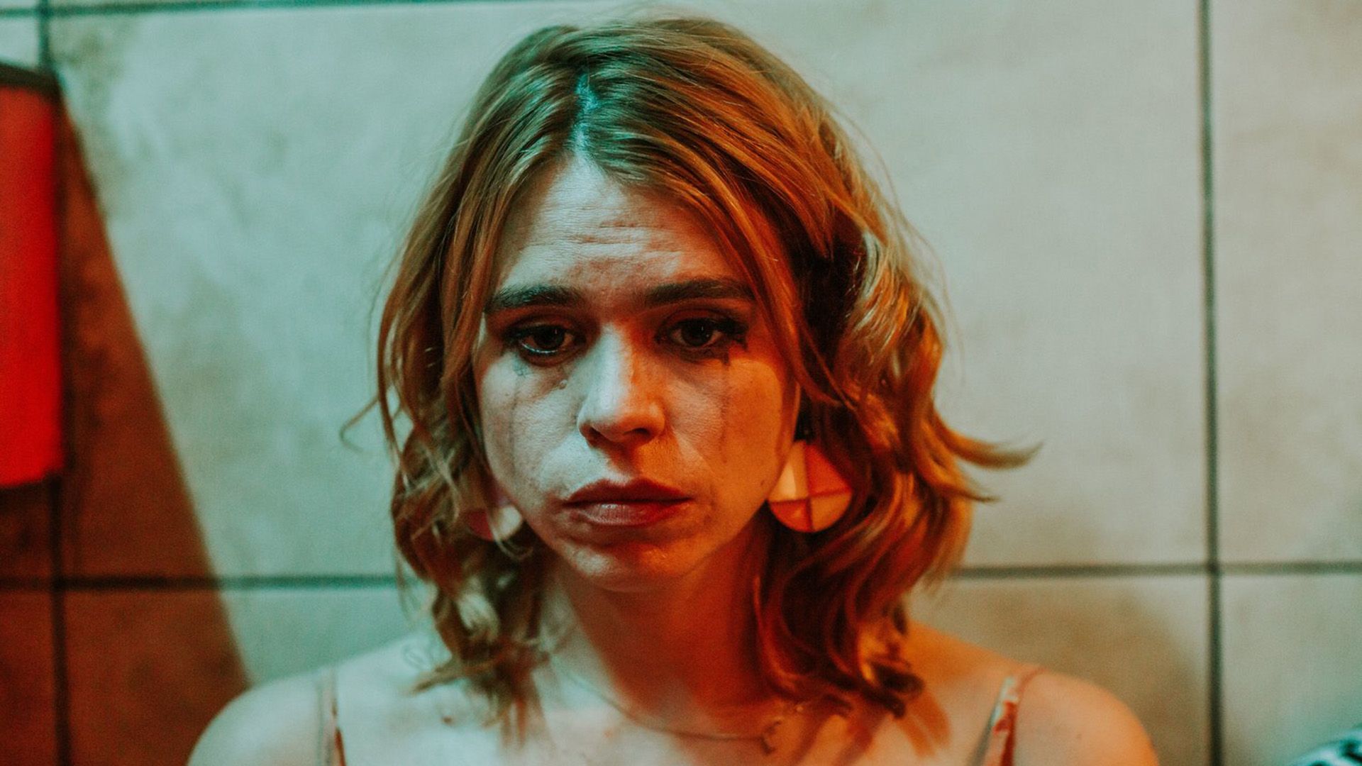 A sad Billie Piper with smudged mascara illuminated by red light