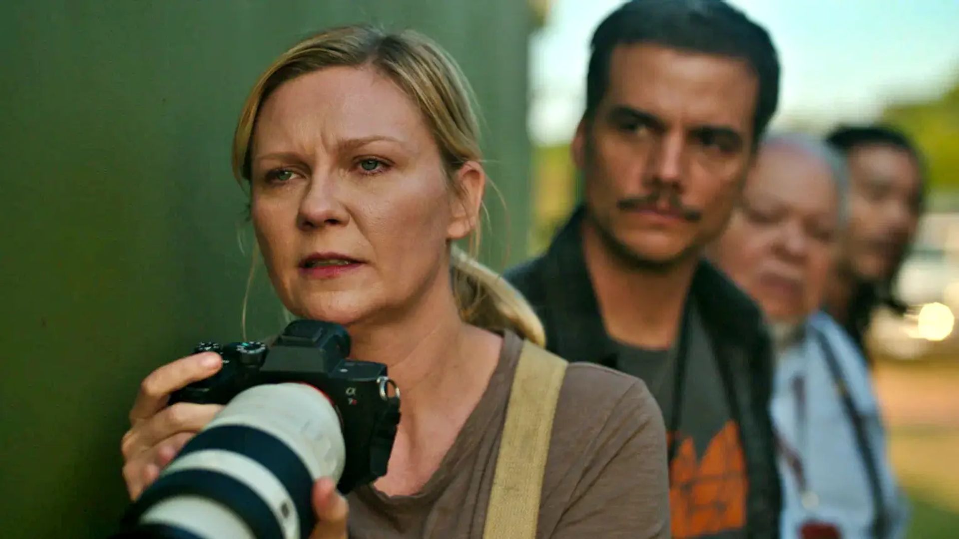 Kirsten Dunst holds a camera and looks ahead with tension