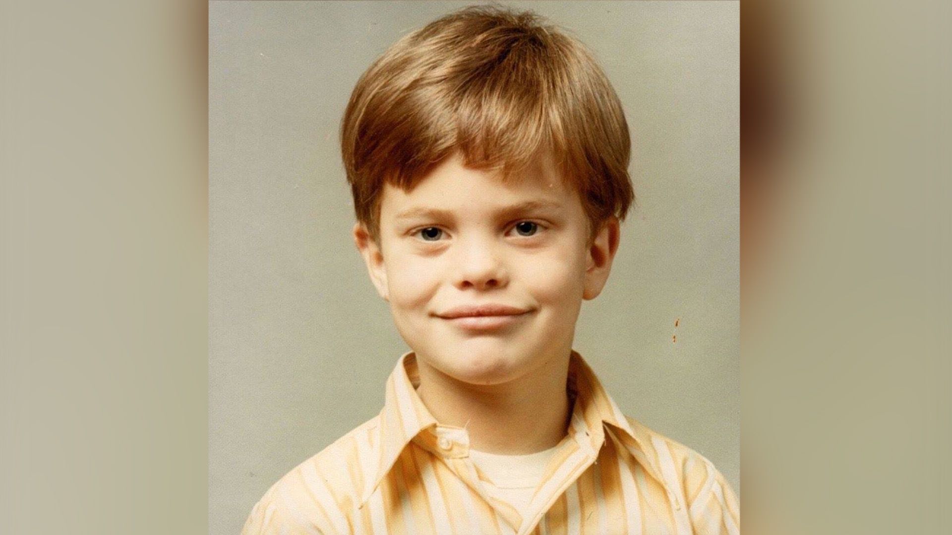 Rainn Wilson as a child in a striped shirt against a beige background