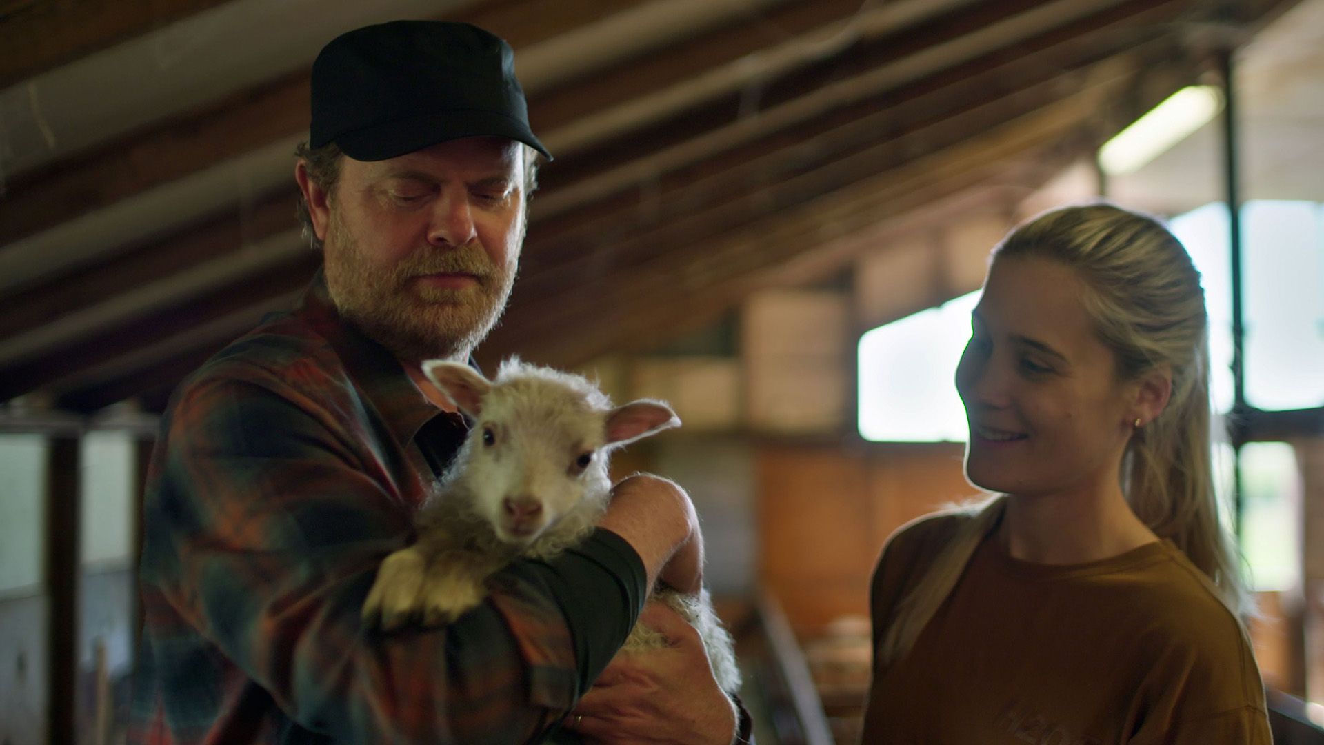 Rainn Wilson holding a baby goat with a smiling girl standing next to him