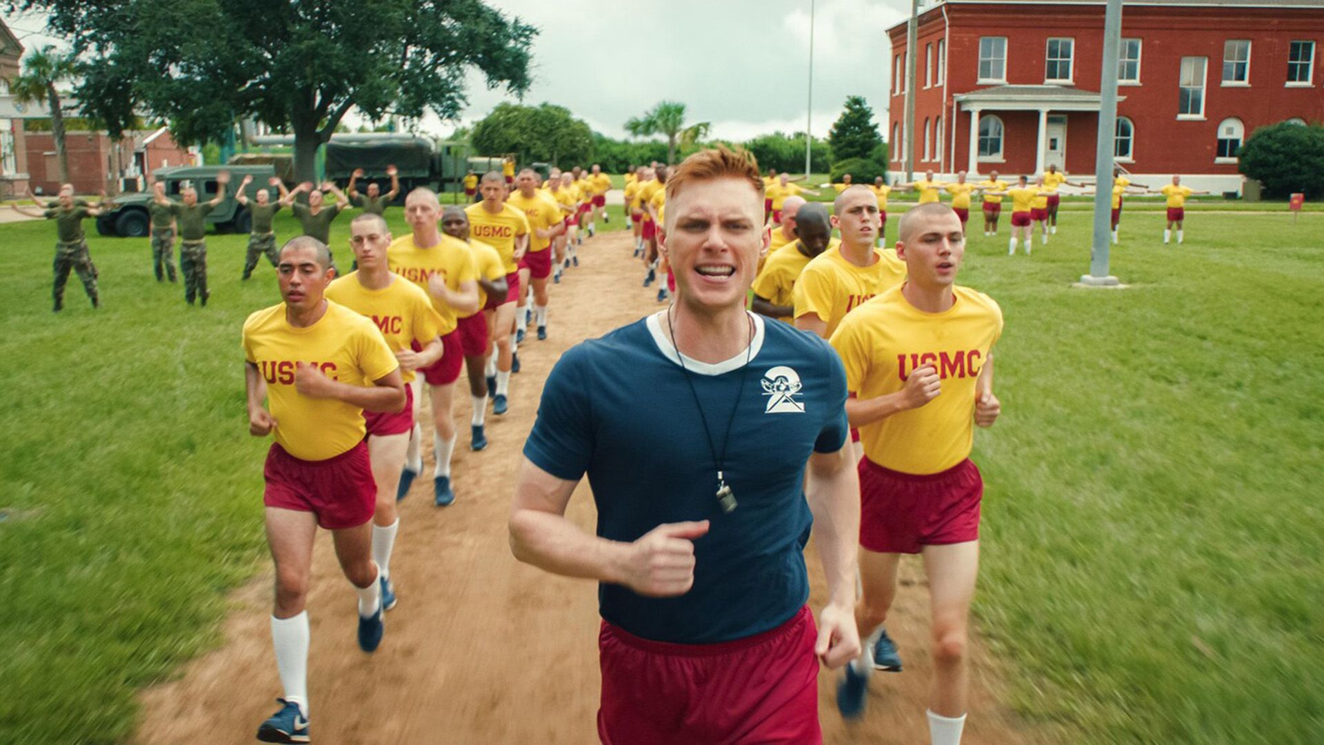 Max Parker in a blue shirt with a whistle around his neck runs down a path followed by a line of young guys in yellow shirts