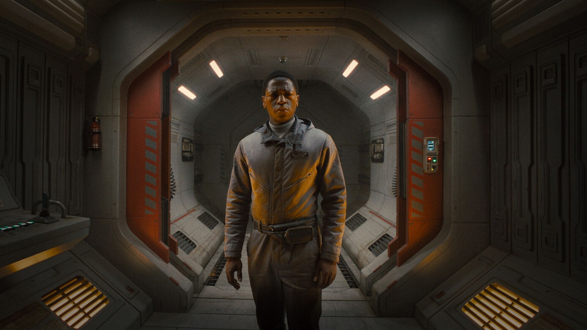 David Jonsson in a gray jumpsuit stands in a spaceship corridor