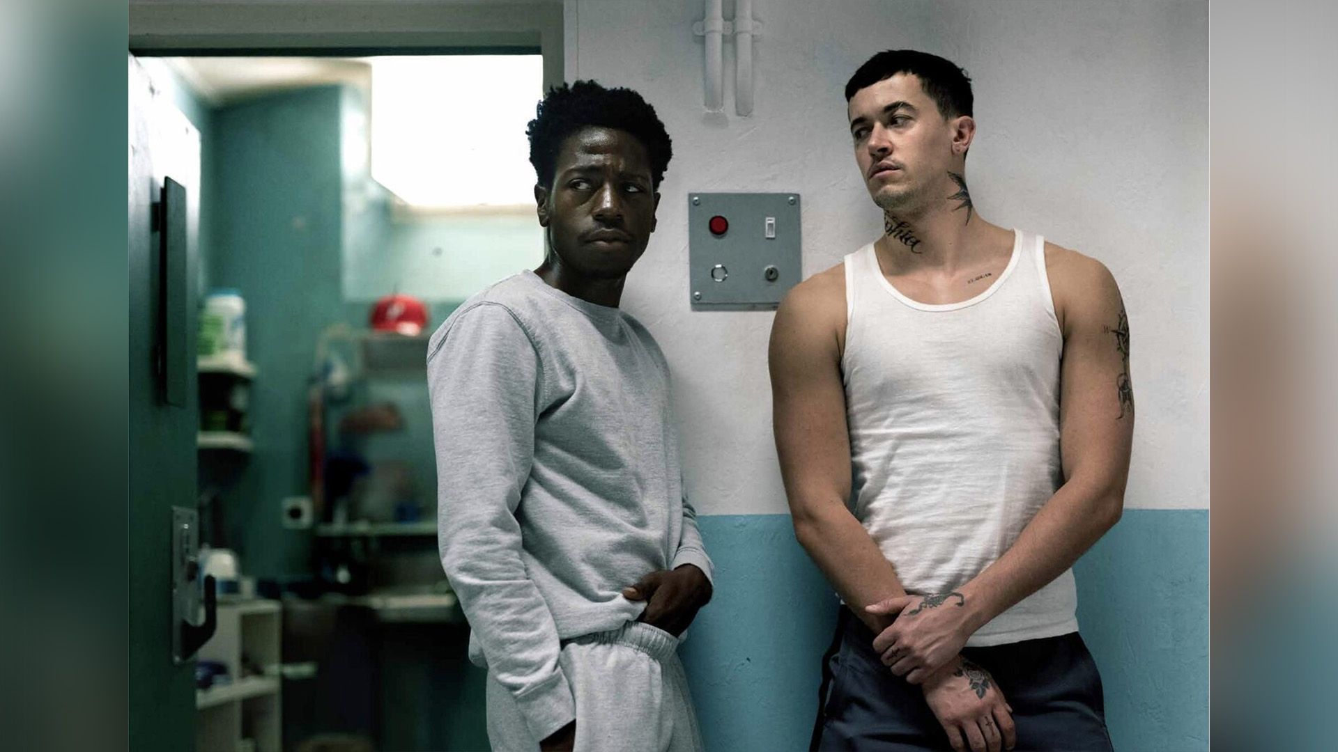David Jonsson in a grey tracksuit stands by a prison cell next to a tall man in a white tank top