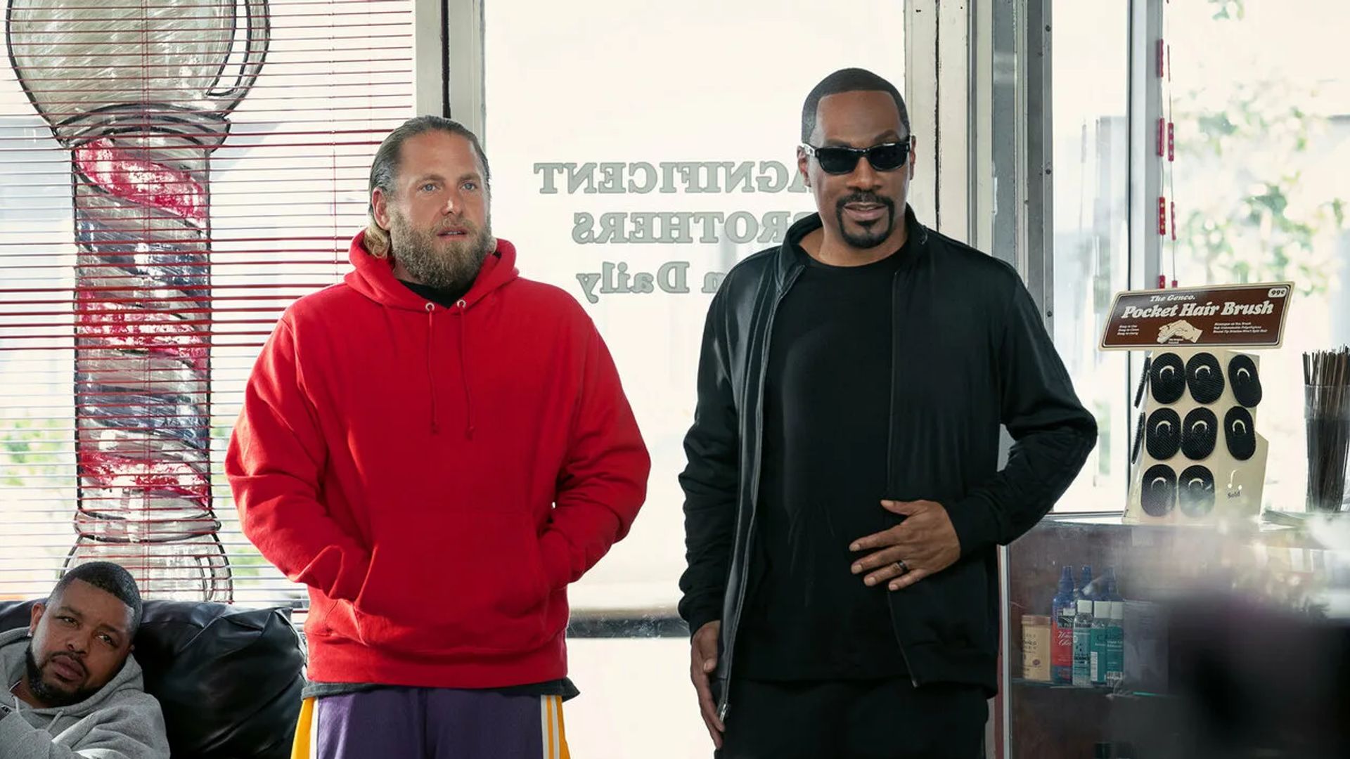 Jonah Hill in a red hoodie and Eddie Murphy in all black standing in a store