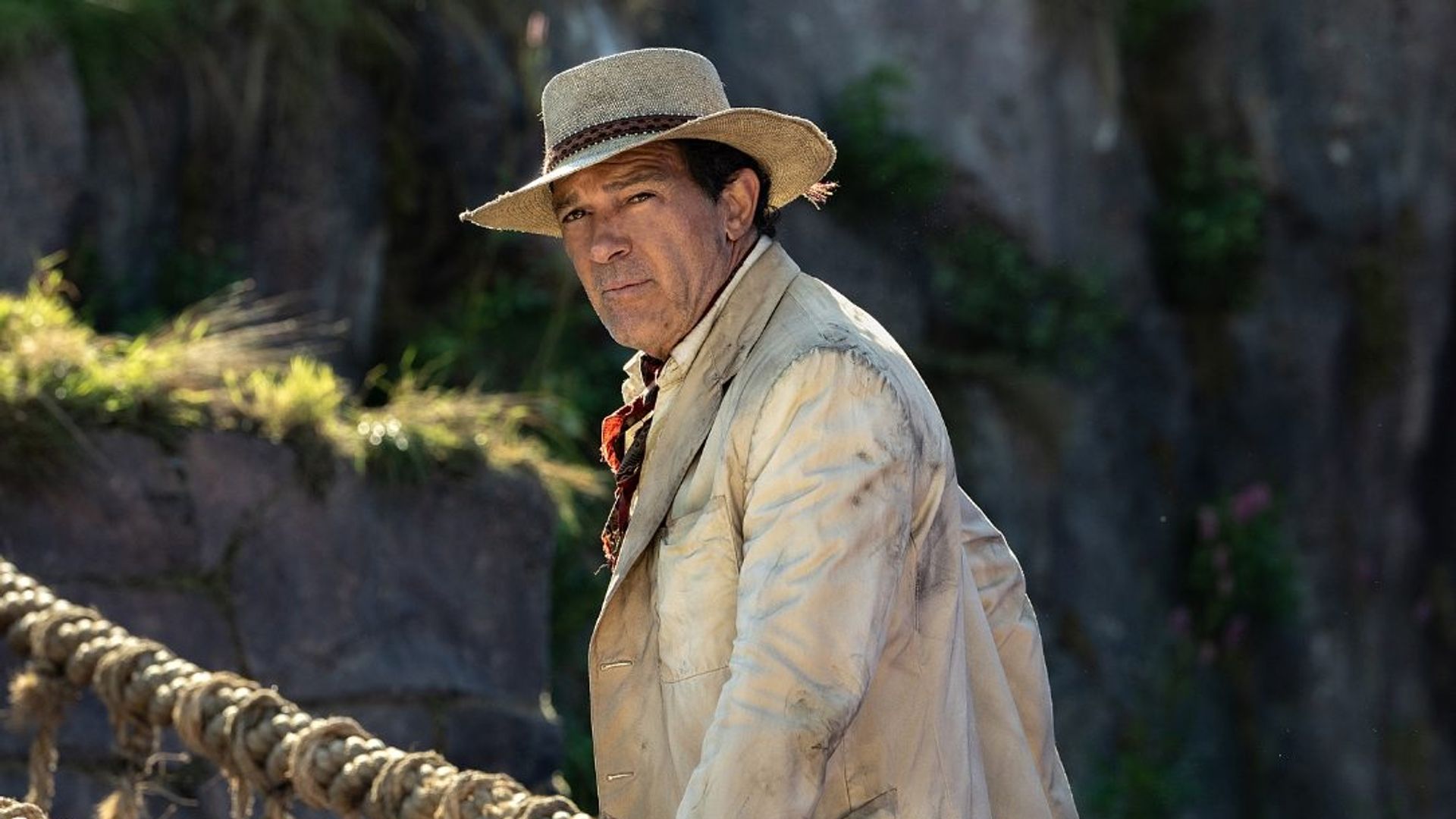 Antonio Banderas in retro adventurer costume against a jungle backdrop with a suspension bridge