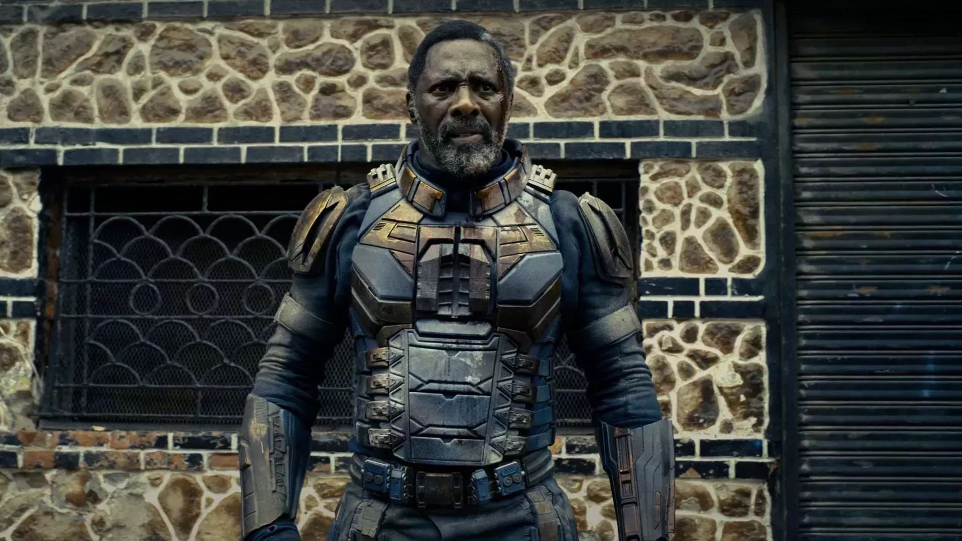Idris Elba in superhero armor against a brick building backdrop