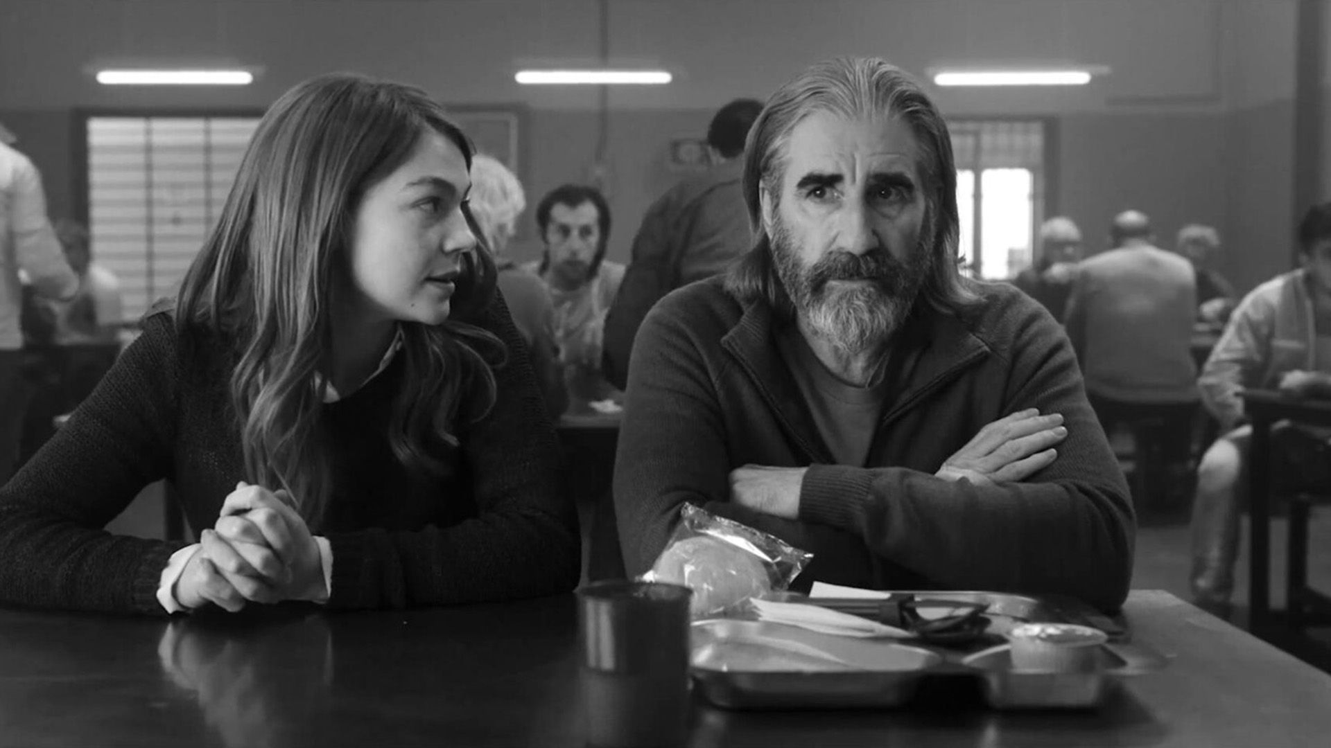 John Lynch sits at a table in the dining hall, a girl sits next to him saying something