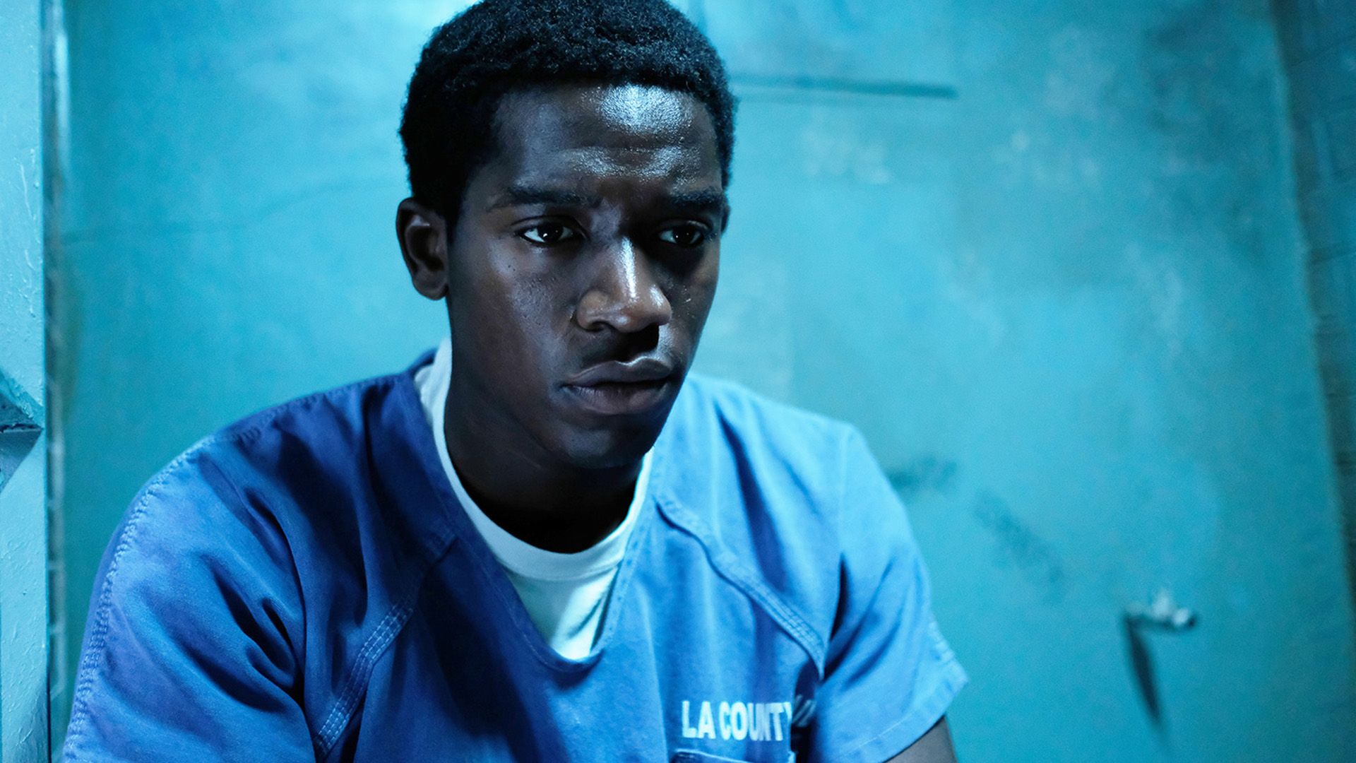 Damson Idris in a blue prison shirt sits in a prison cell