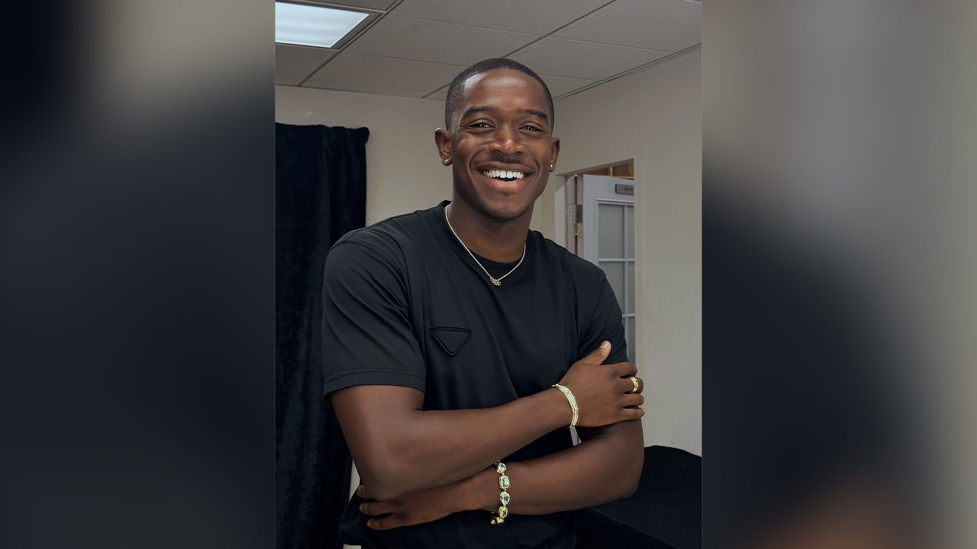 Damson Idris wearing a black t-shirt smiles broadly