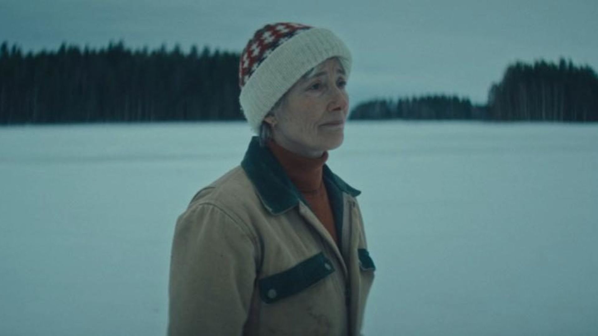 Emma Thompson in winter clothing stands against a snowy backdrop, blue-tinted photo