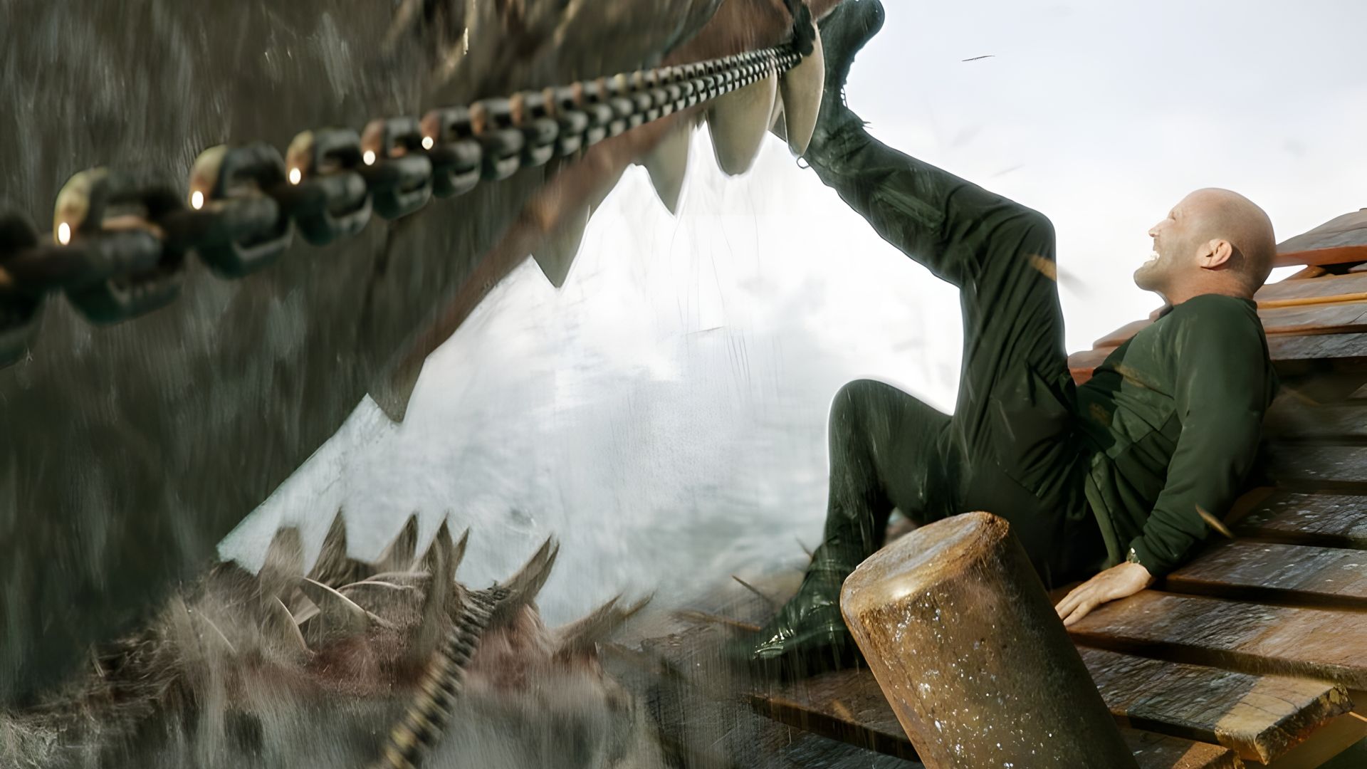 Jason Statham in black clothing kicks off a massive shark with its jaws wide open at the water's surface