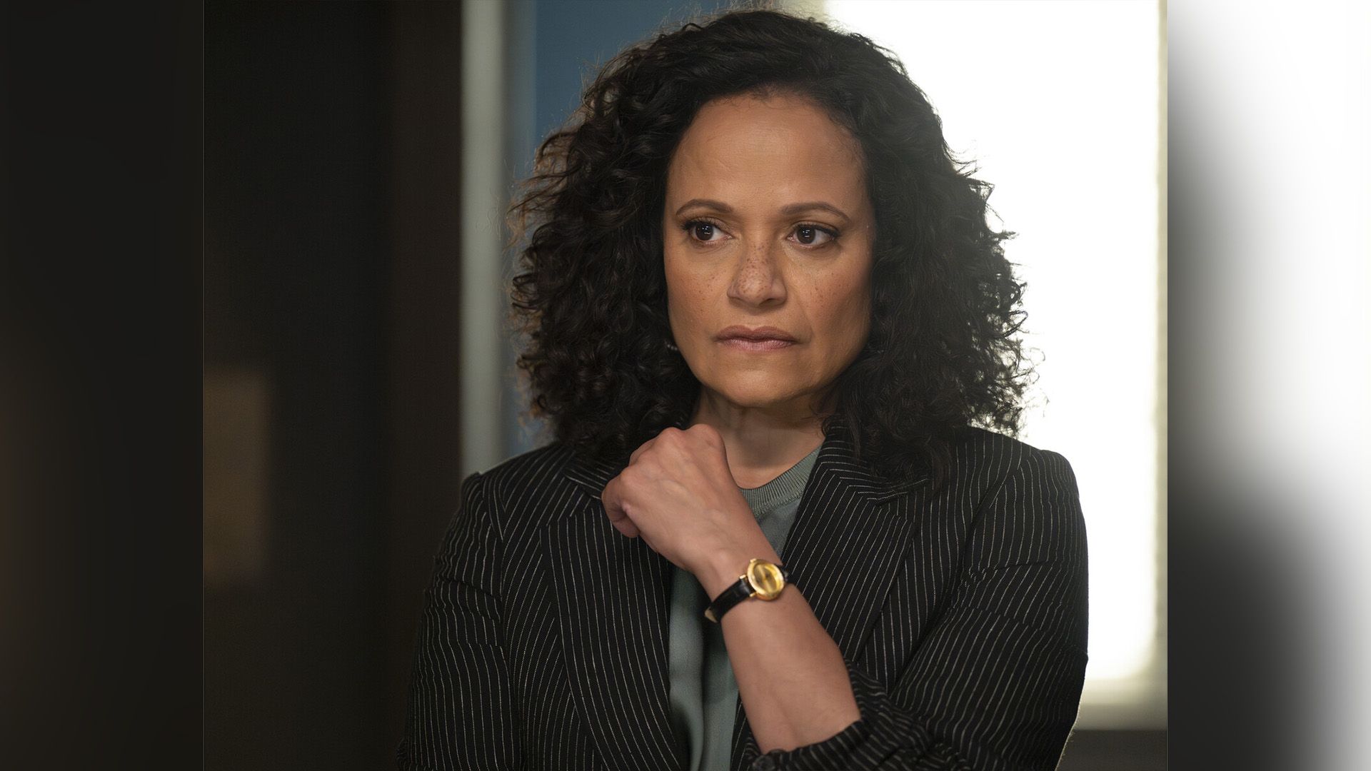 Judy Reyes in a striped blazer gazes thoughtfully to the side