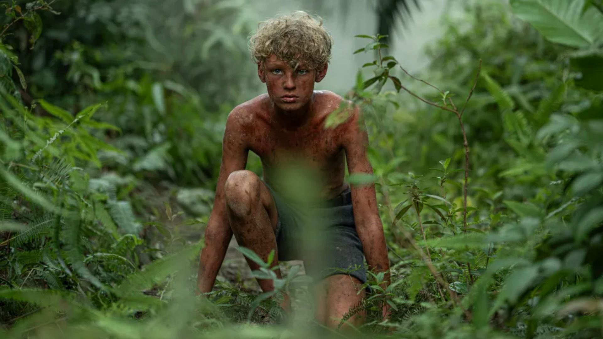 A boy with dirty skin sits in the grass looking at the camera