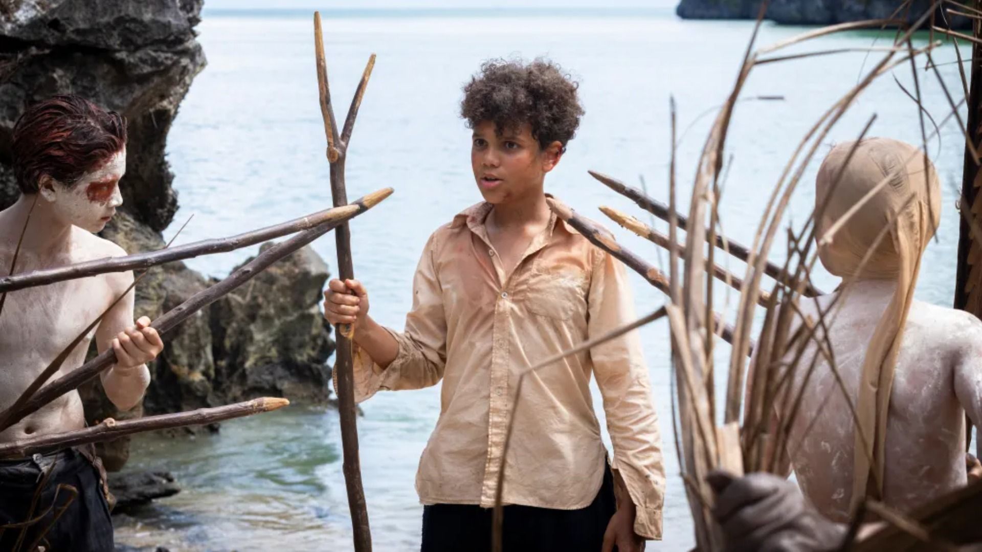 Children in white shirts with white body paint holding wooden spears