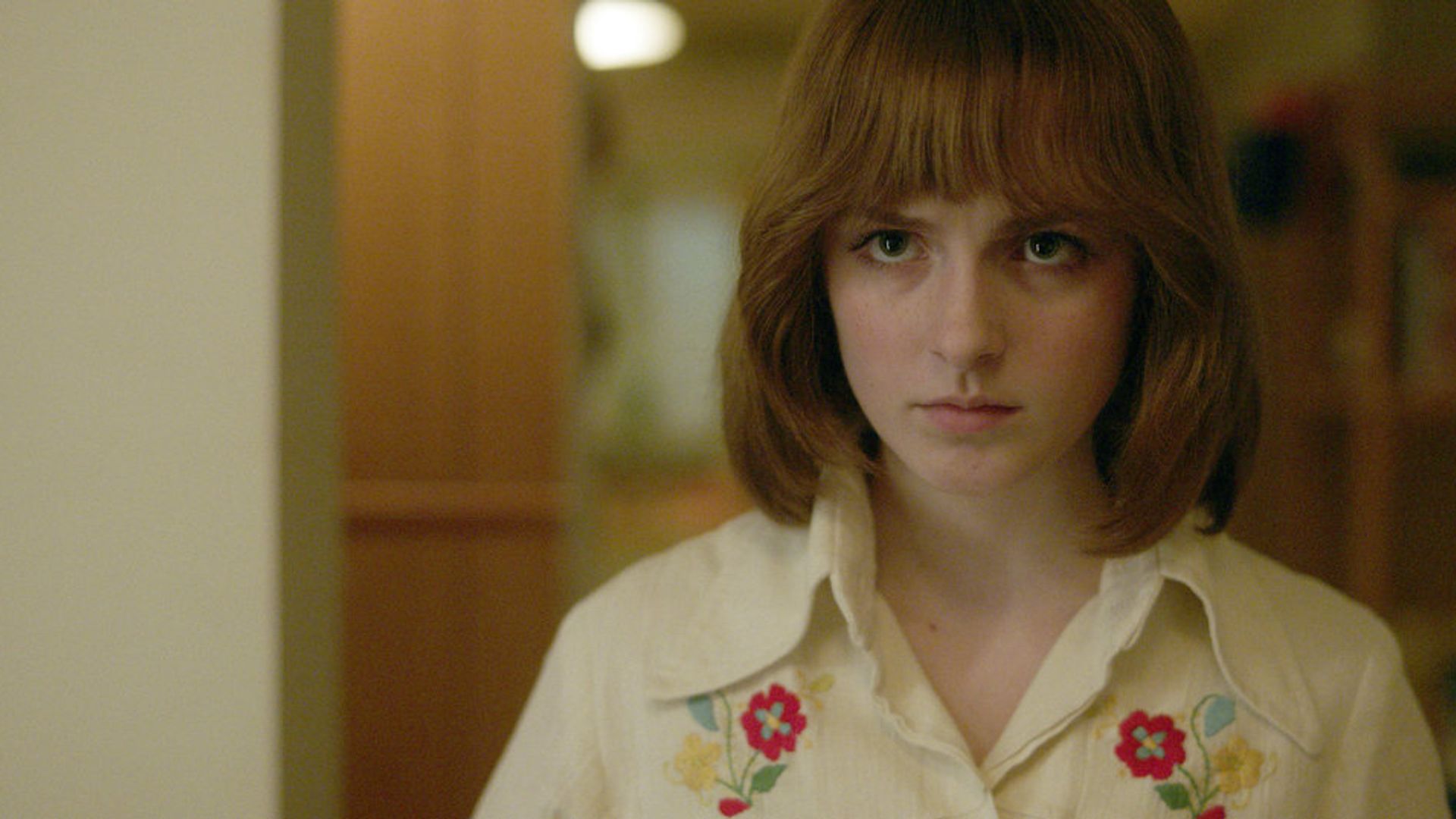 Mckenna Grace with a red bob haircut and 80s fashion, a scene from the miniseries