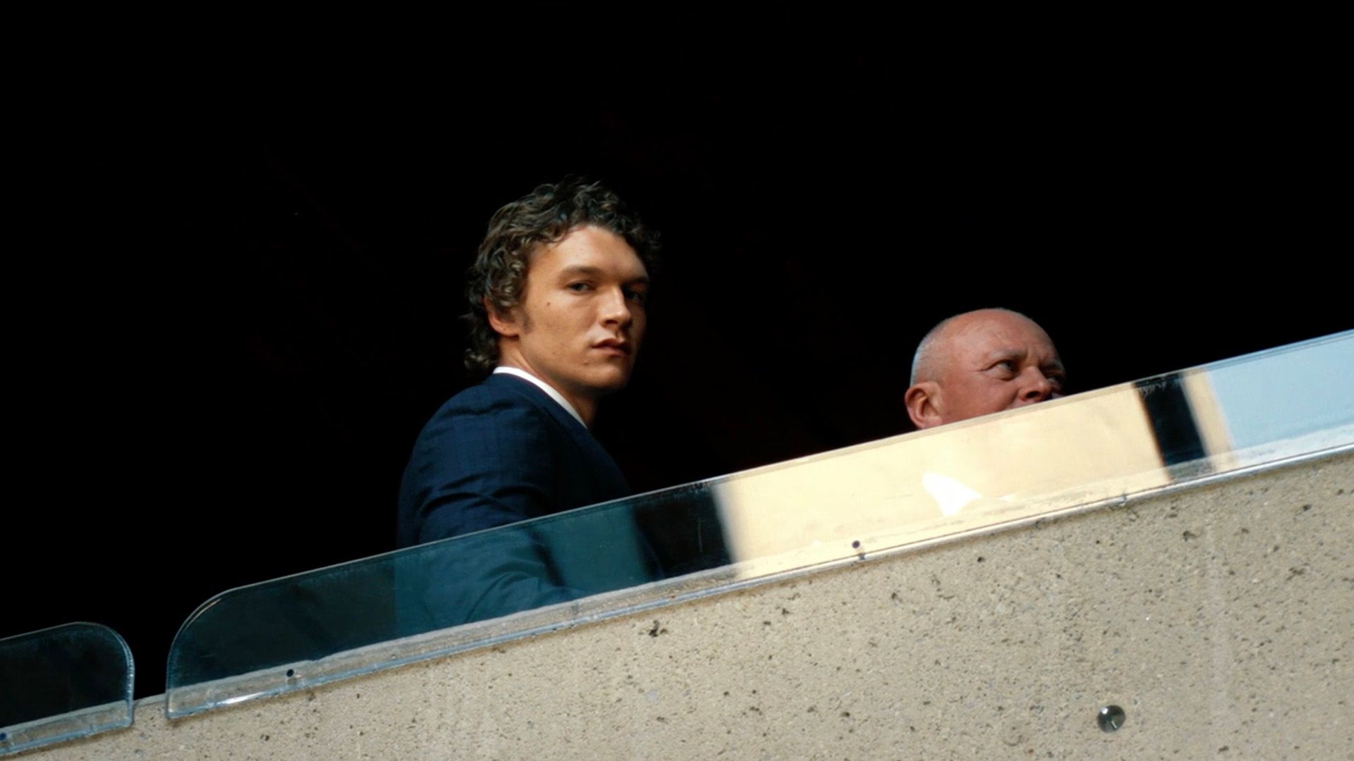 Connor Storrie in a blazer gazing thoughtfully down from a balcony