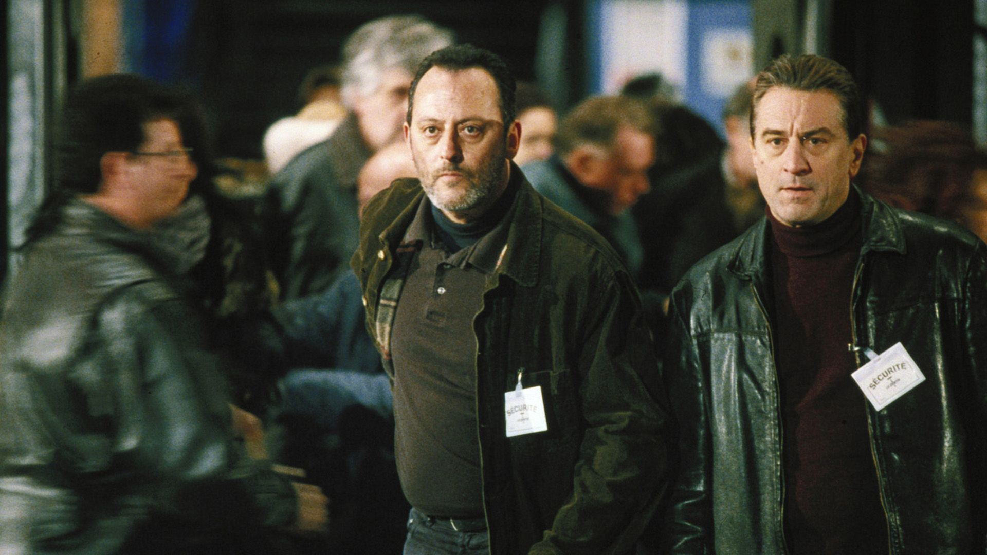 Jean Reno and Robert De Niro in black with badges that say "security" on their chests