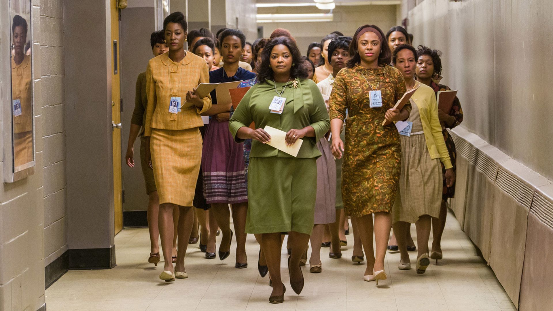 A group of dark-skinned women in 1960s clothing walking down the hallway