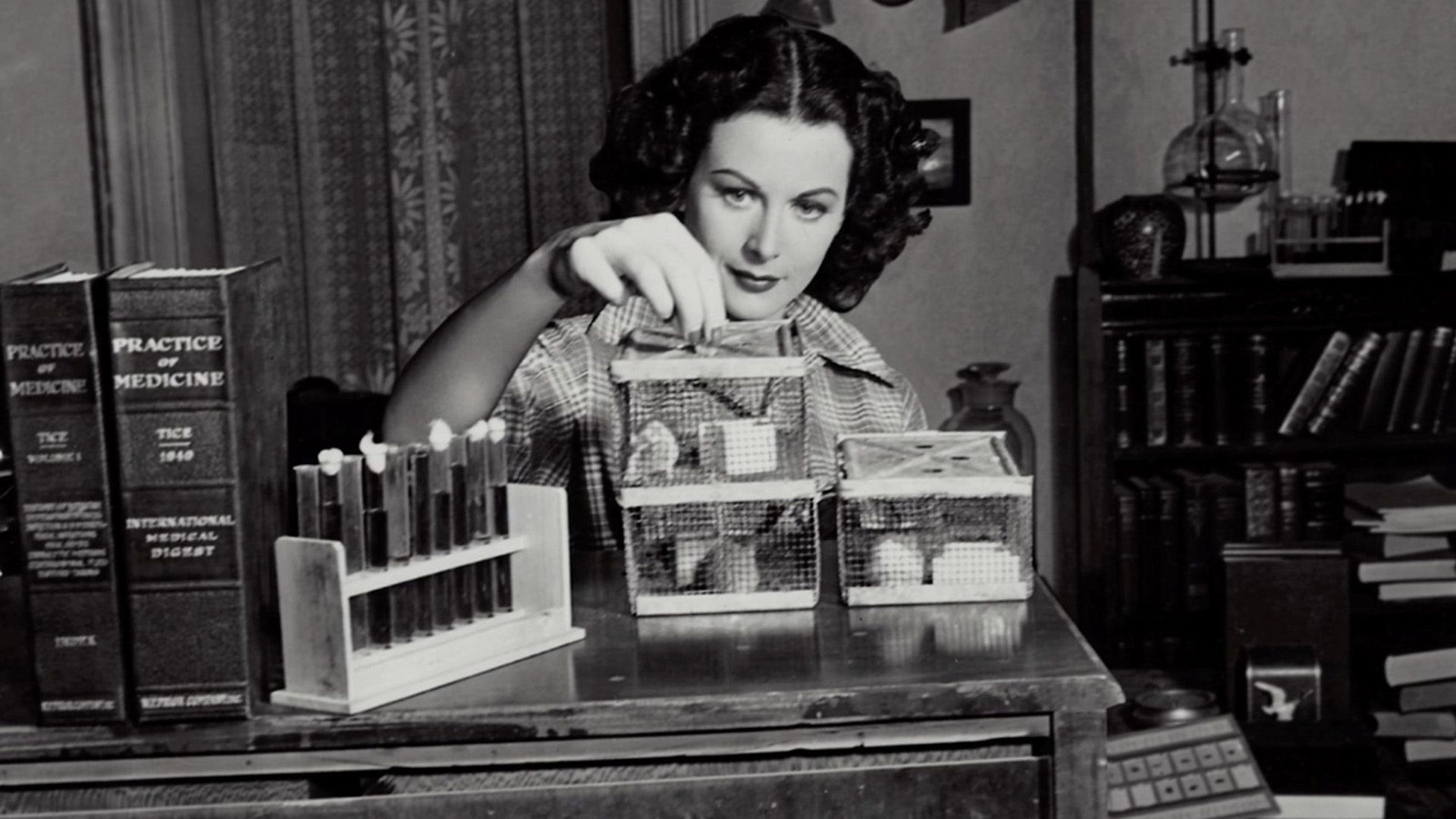 A young beautiful woman is looking at cages with mice, next to her on the table are test tubes and books on medicine