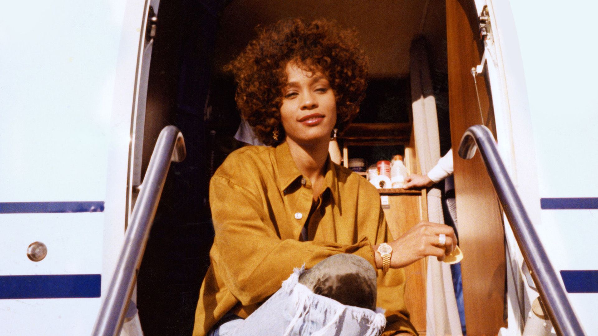 A young dark-skinned woman with curls sitting on the steps at the entrance of a private jet