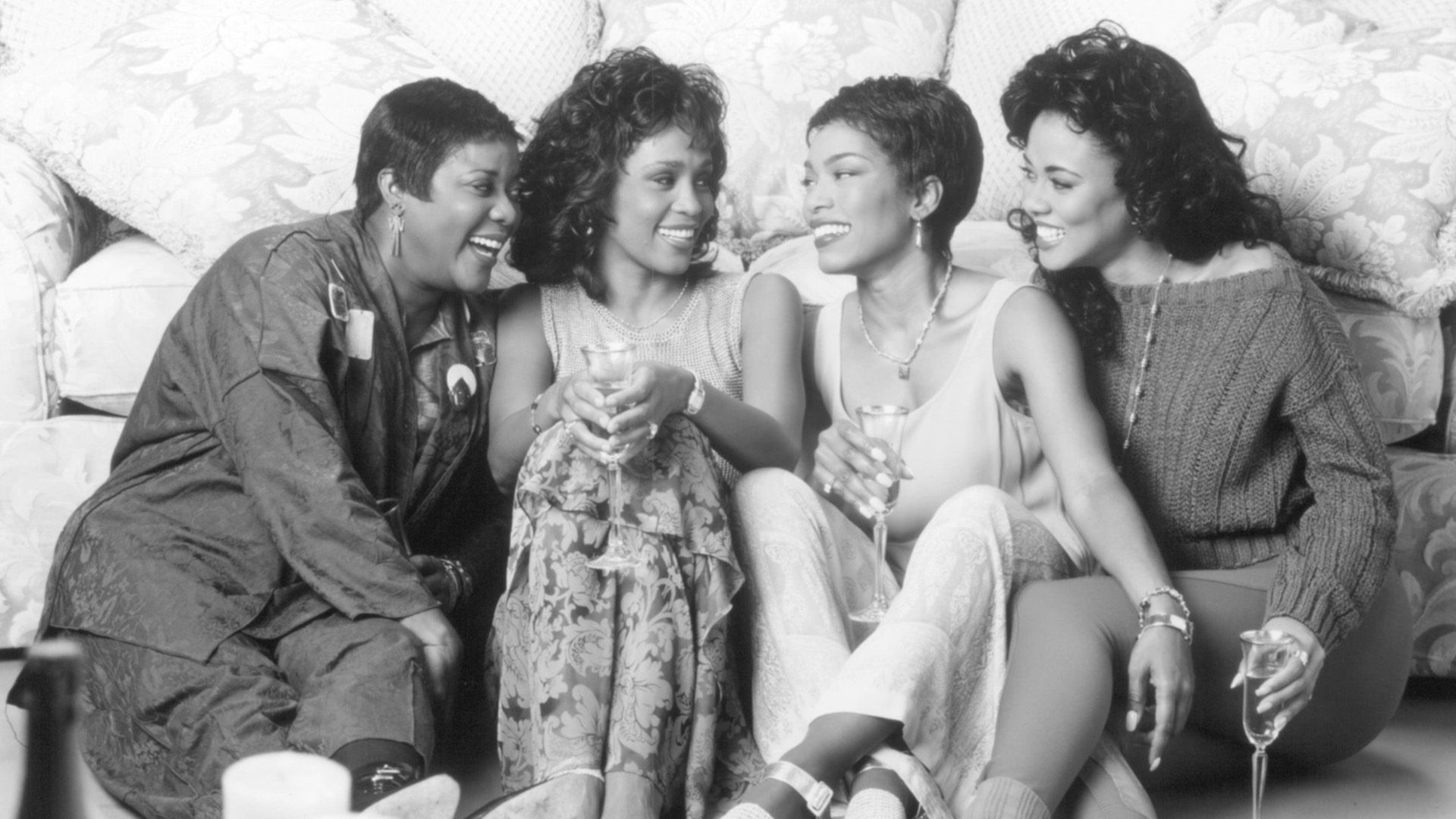 Four dark-skinned women sitting on the floor by the sofa and laughing