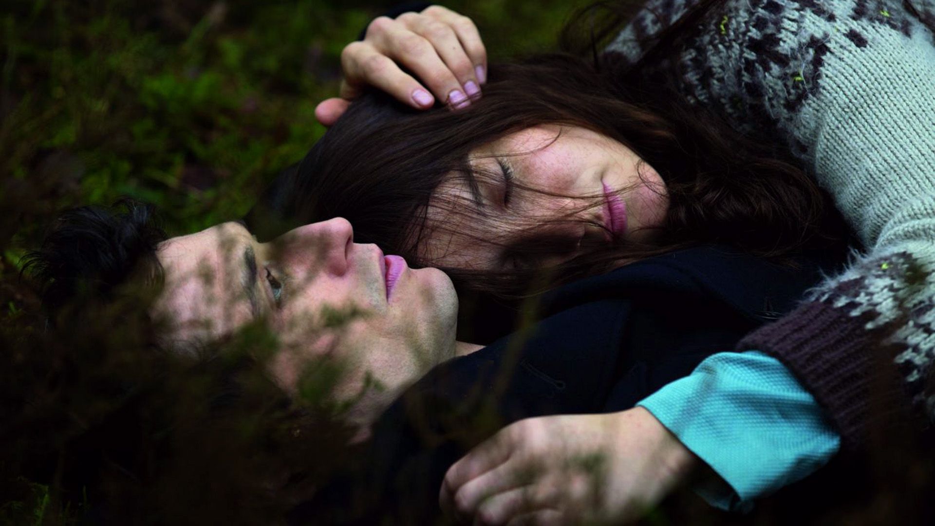 Close-up: a young man and a girl are lying in the grass embraced