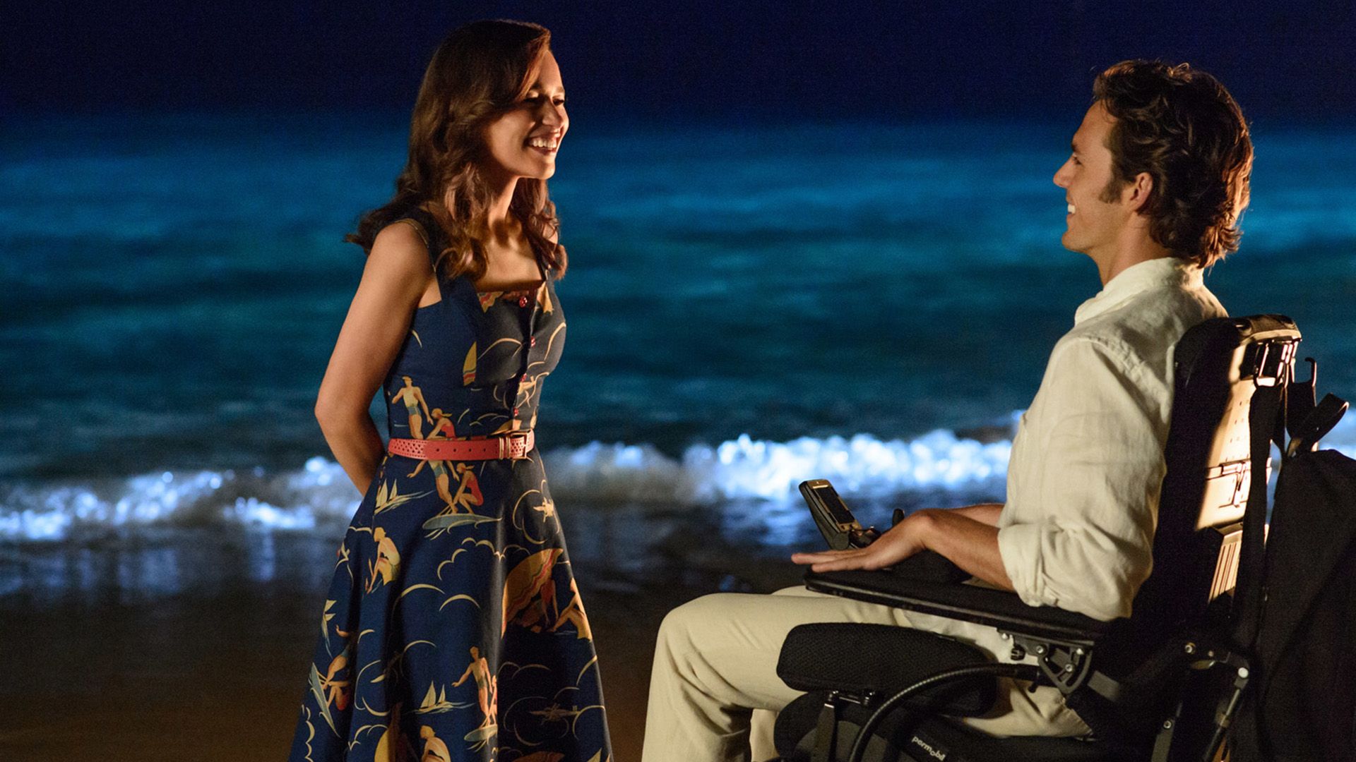 Evening, beach, a young girl in a colorful dress stands in front of a young man in a wheelchair, both smiling