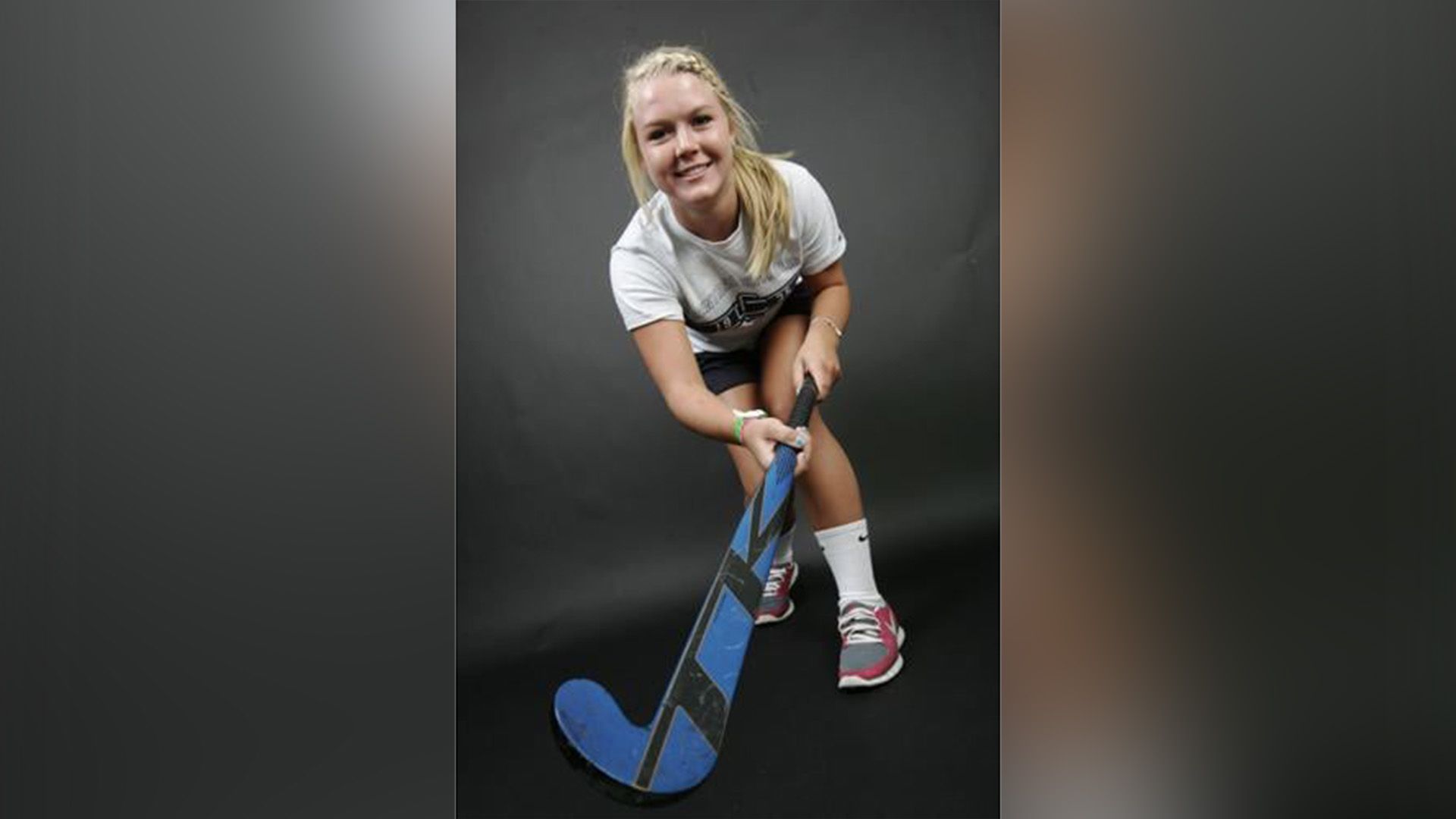 A young smiling girl with a hockey stick against a black background