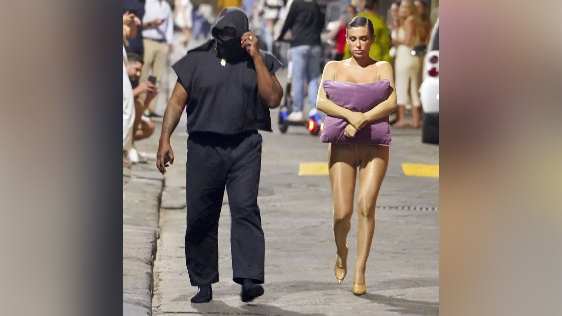 A dark-skinned man in black and a girl in a flesh-colored jumpsuit with a lilac pillow in her hands