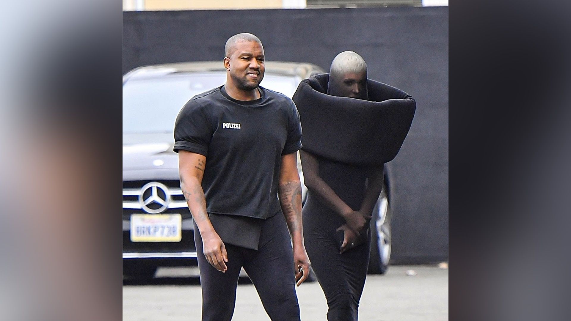 A dark-skinned man in black and a girl in a strange black outfit