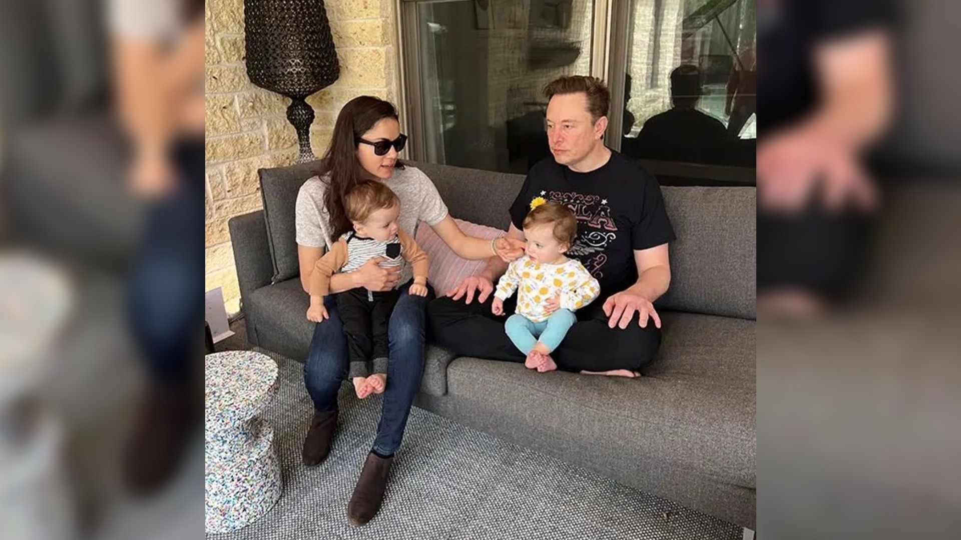 Elon Musk and Shivon Zilis are sitting in chairs on the porch, each holding a baby