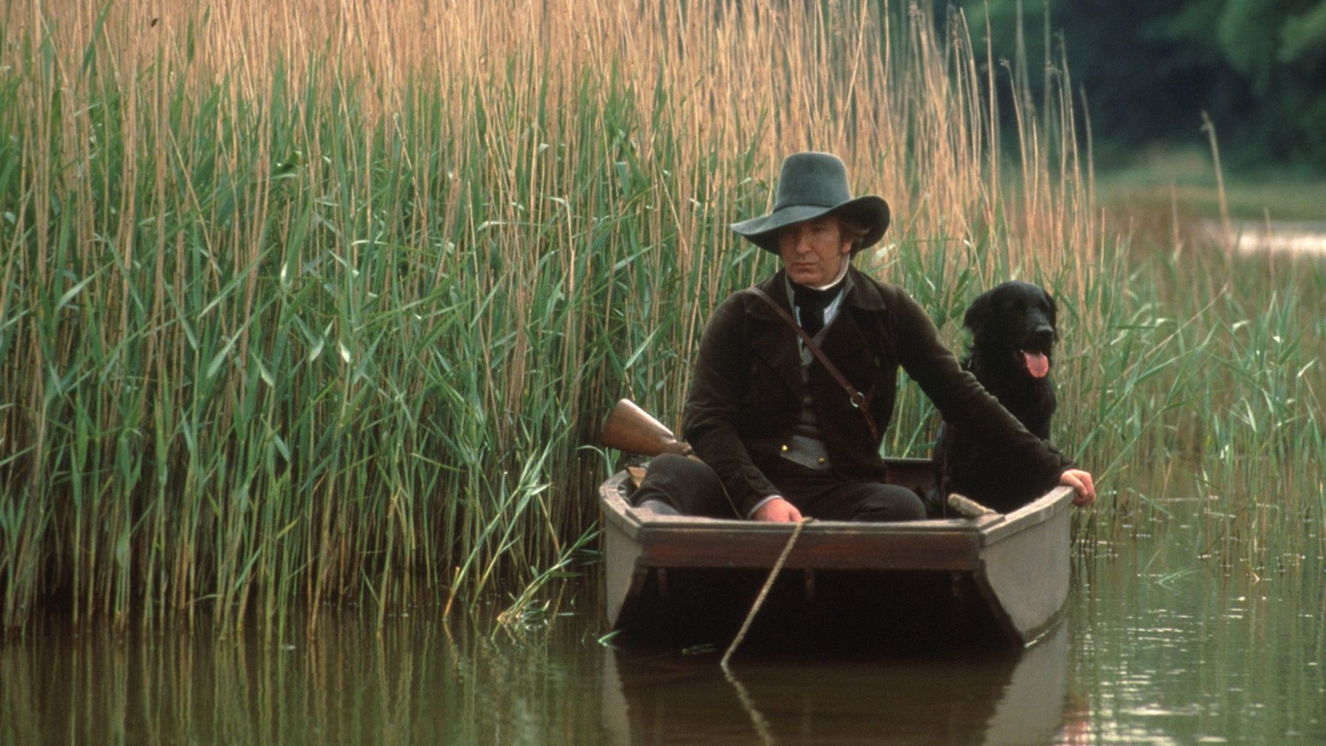 A man in a wide-brimmed hat sits in a boat with a dog among tall reeds