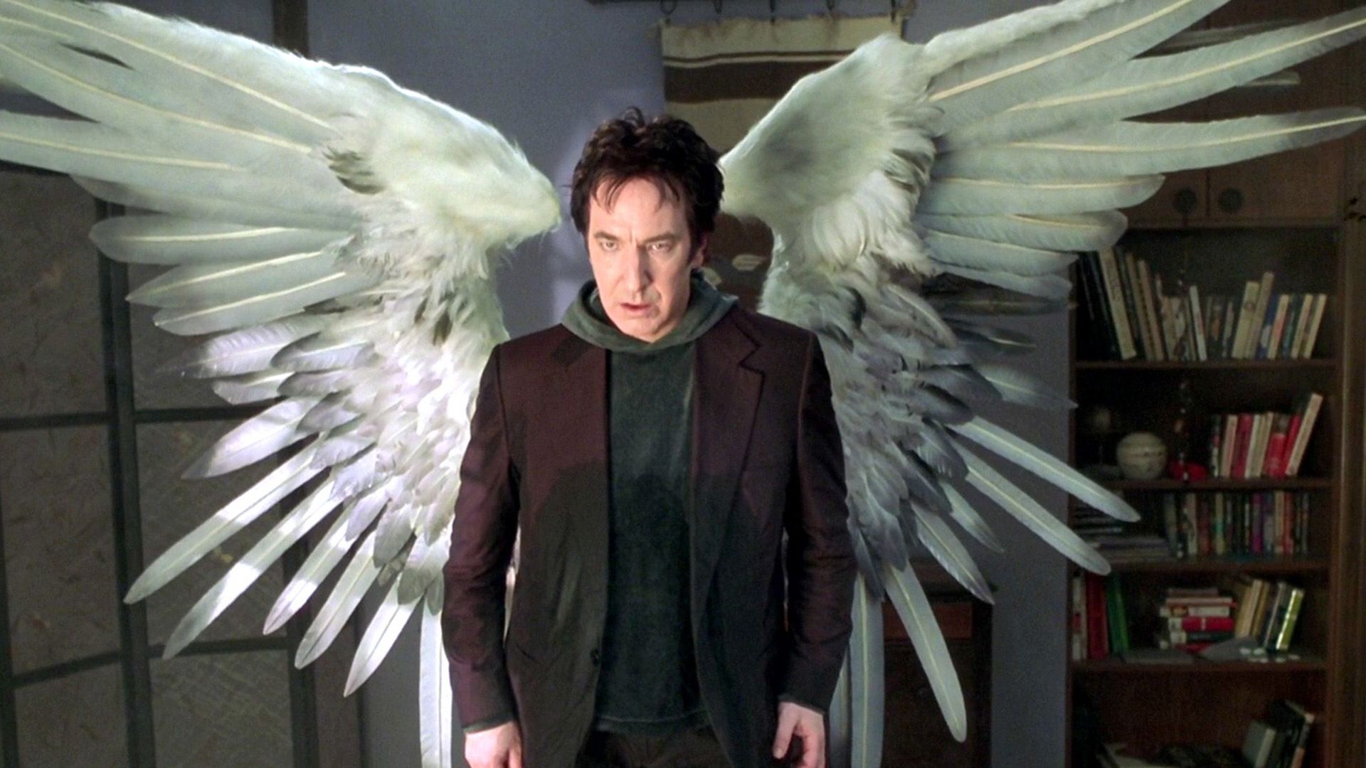 A serious dark-haired man in a black jacket with large white wings behind him