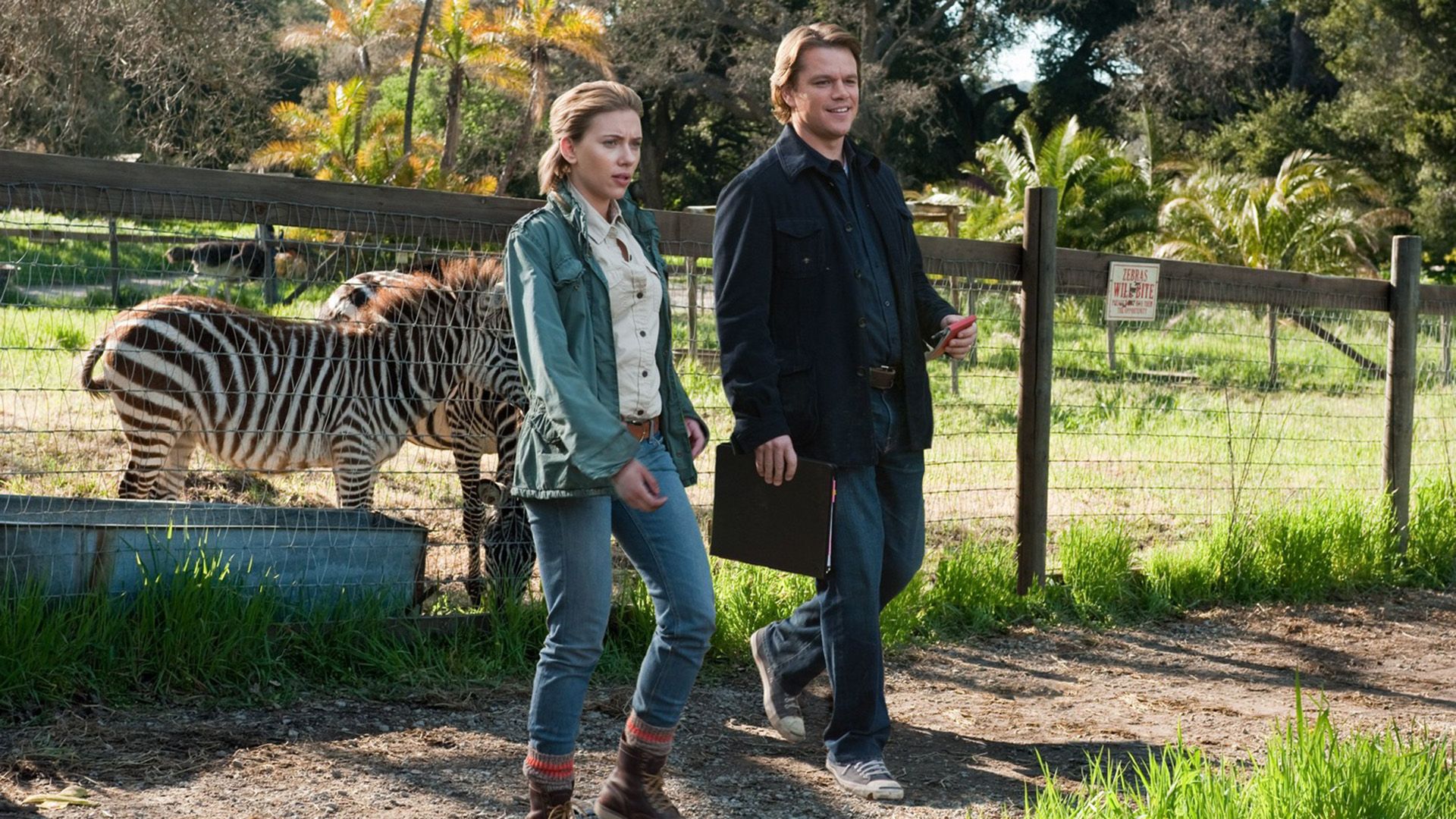 A man and a woman next to the enclosure with zebras