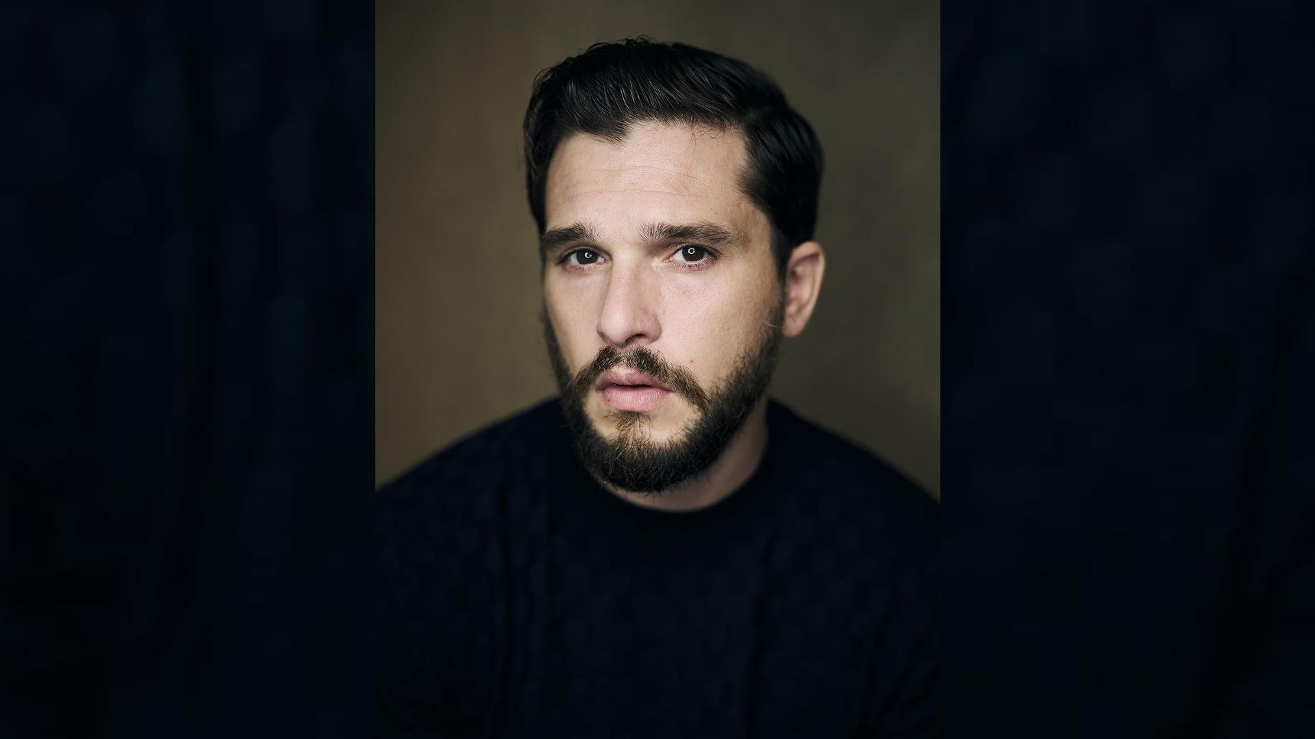 Portrait of actor Kit Harington: he's wearing a black t-shirt, stylish haircut, neat beard