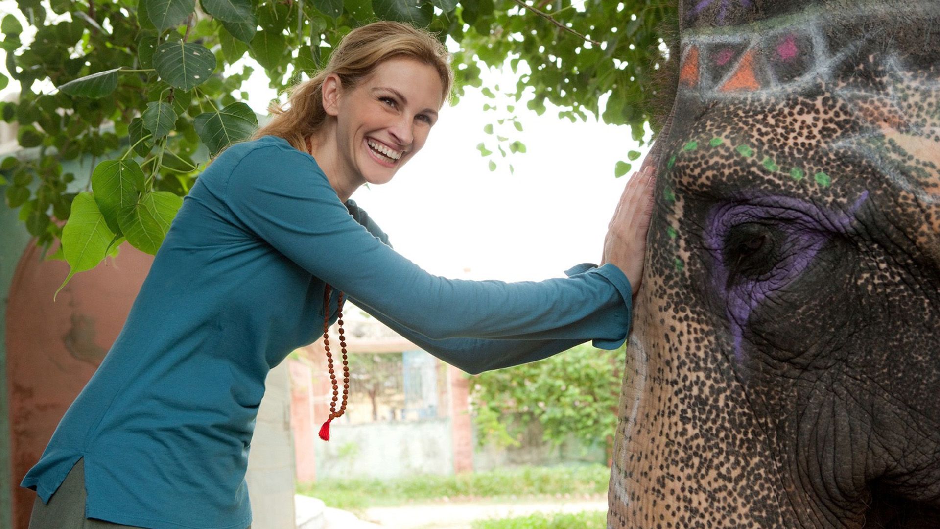 A laughing woman in a green sweater is stroking an elephant on the trunk