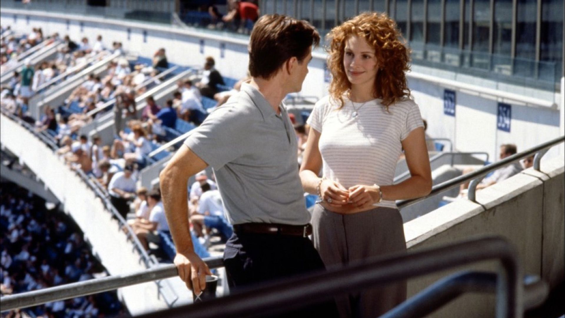 A man and a girl are standing on the balcony of a sports stadium