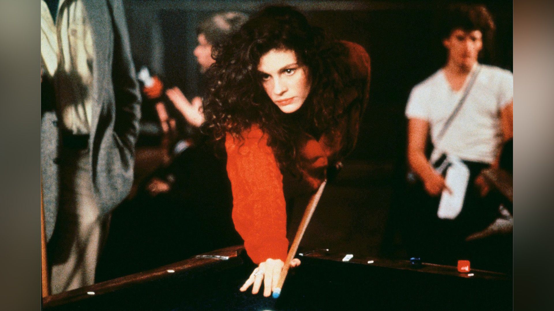 A young curly-haired girl in a red sweater leaned over the billiard table with a cue in her hands