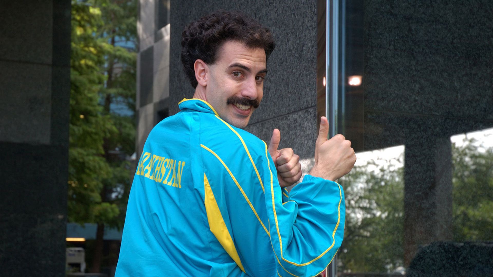 A curly brunette in a blue windbreaker shows thumbs up and smiles broadly